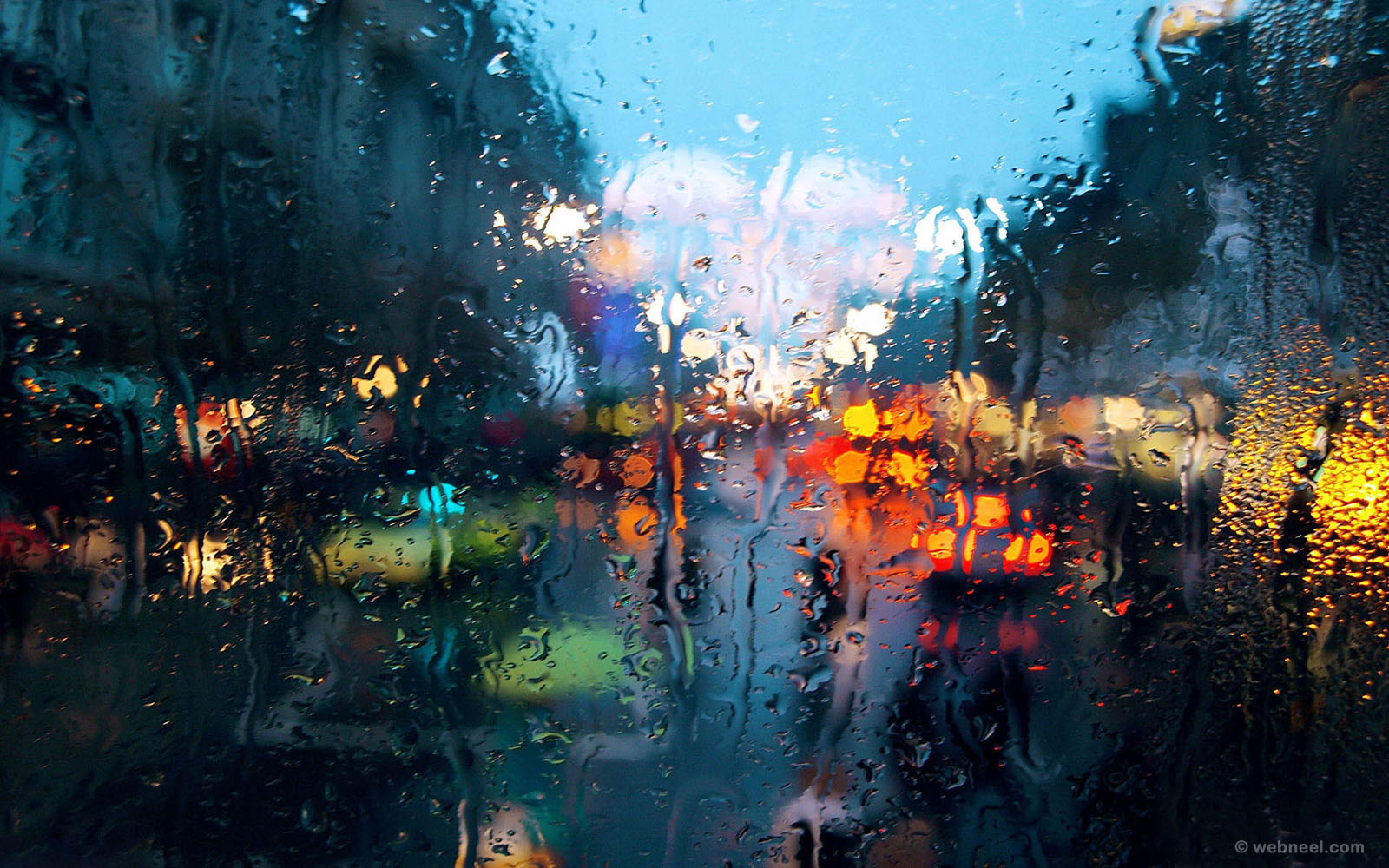 Raindrops on a window pane blur the city lights in the background, creating a dreamy and atmospheric rainy scene
