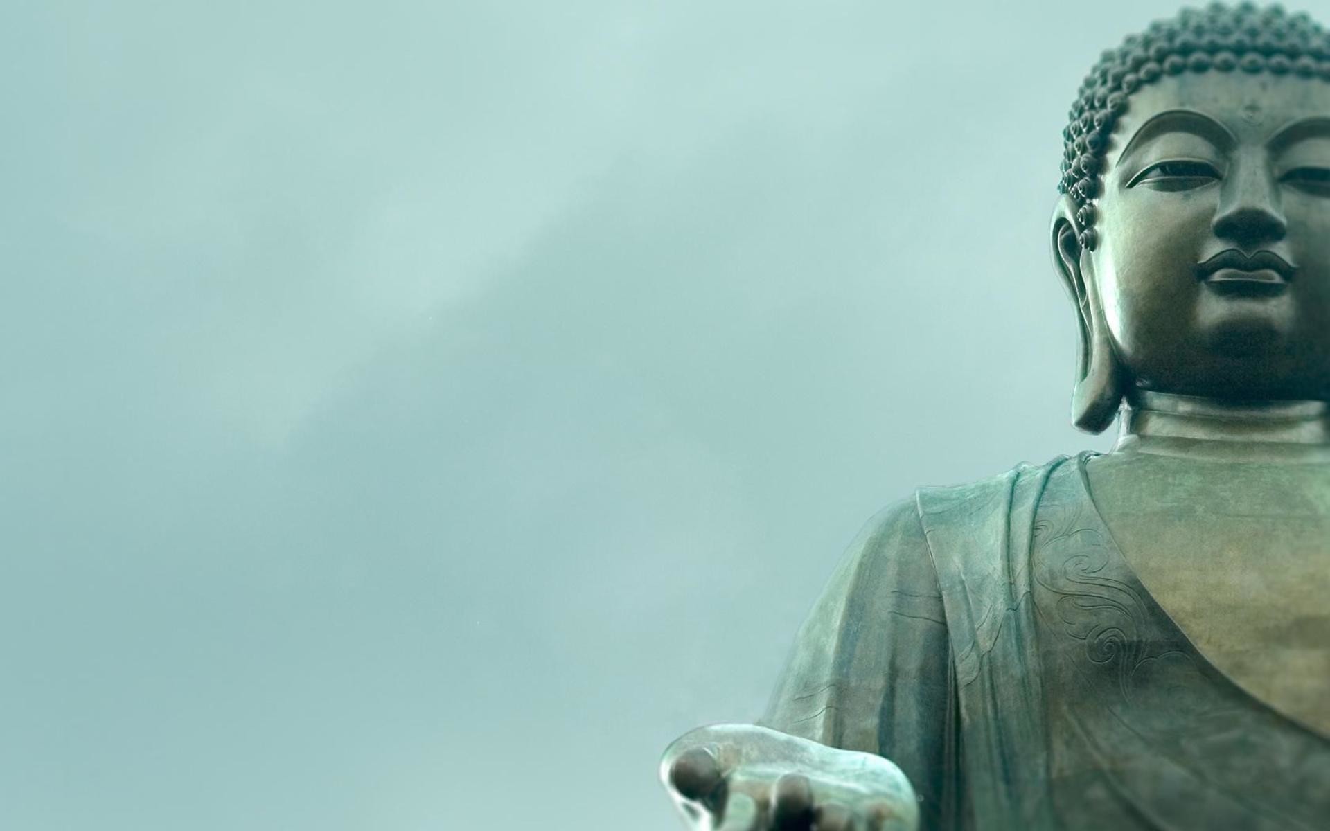 Serene close-up of the Tian Tan Buddha statue against a misty sky. The statue's face and hand gesture evoke peace and tranquility
