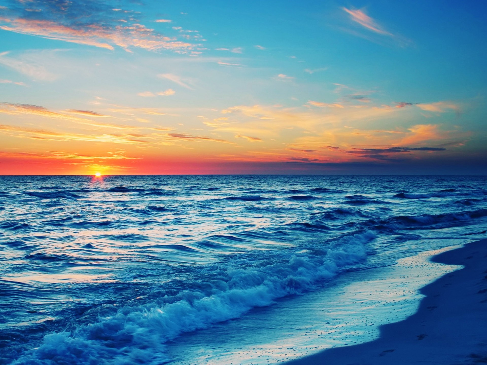 Vivid sunset over a tranquil ocean with gentle waves lapping at the sandy shore
