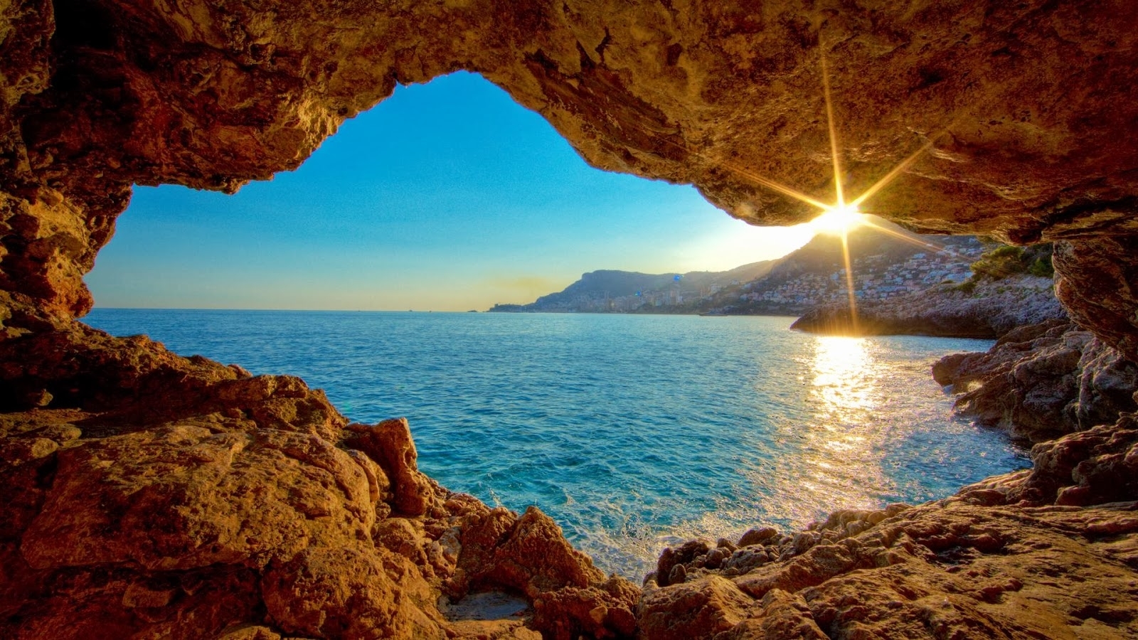 Sunset view from inside a sea cave, overlooking the Mediterranean Sea. The warm light of the setting sun illuminates the rocky cave walls and casts a golden glow on the water