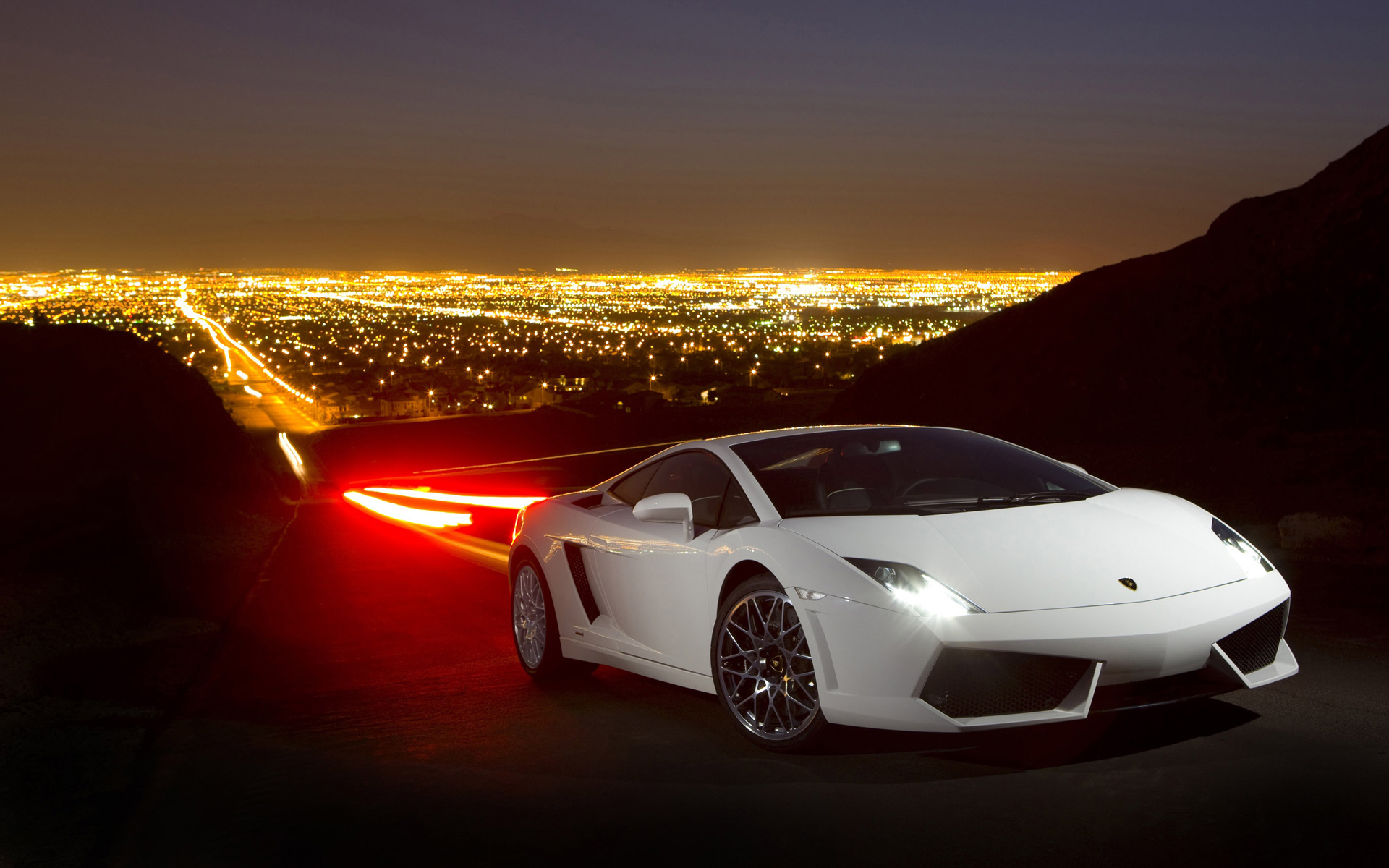 A white Lamborghini Gallardo parked overlooking a cityscape at night