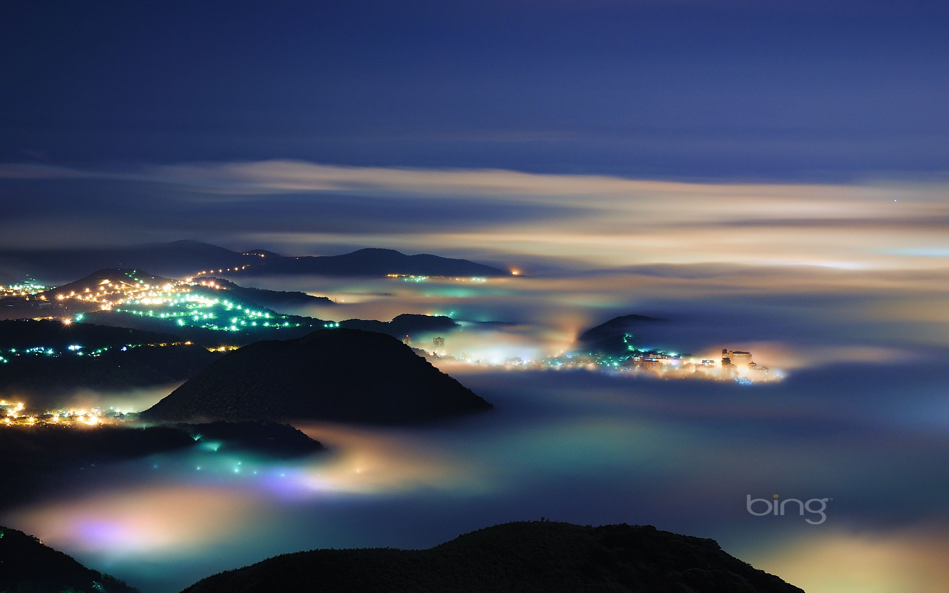 Stunning wallpaper of a city nestled in the mountains, shrouded in fog at night