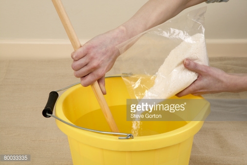 Pouring Wallpaper Paste In To A Bucket Of Water And Stirring With