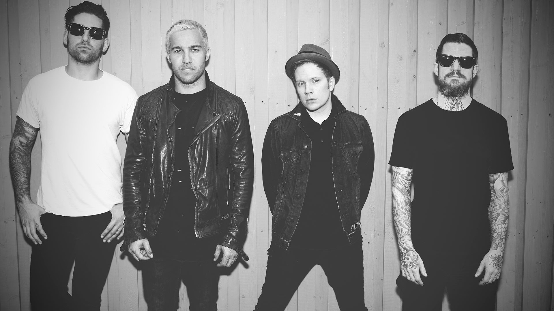 A black and white photo of the band Fall Out Boy posing against a wooden wall