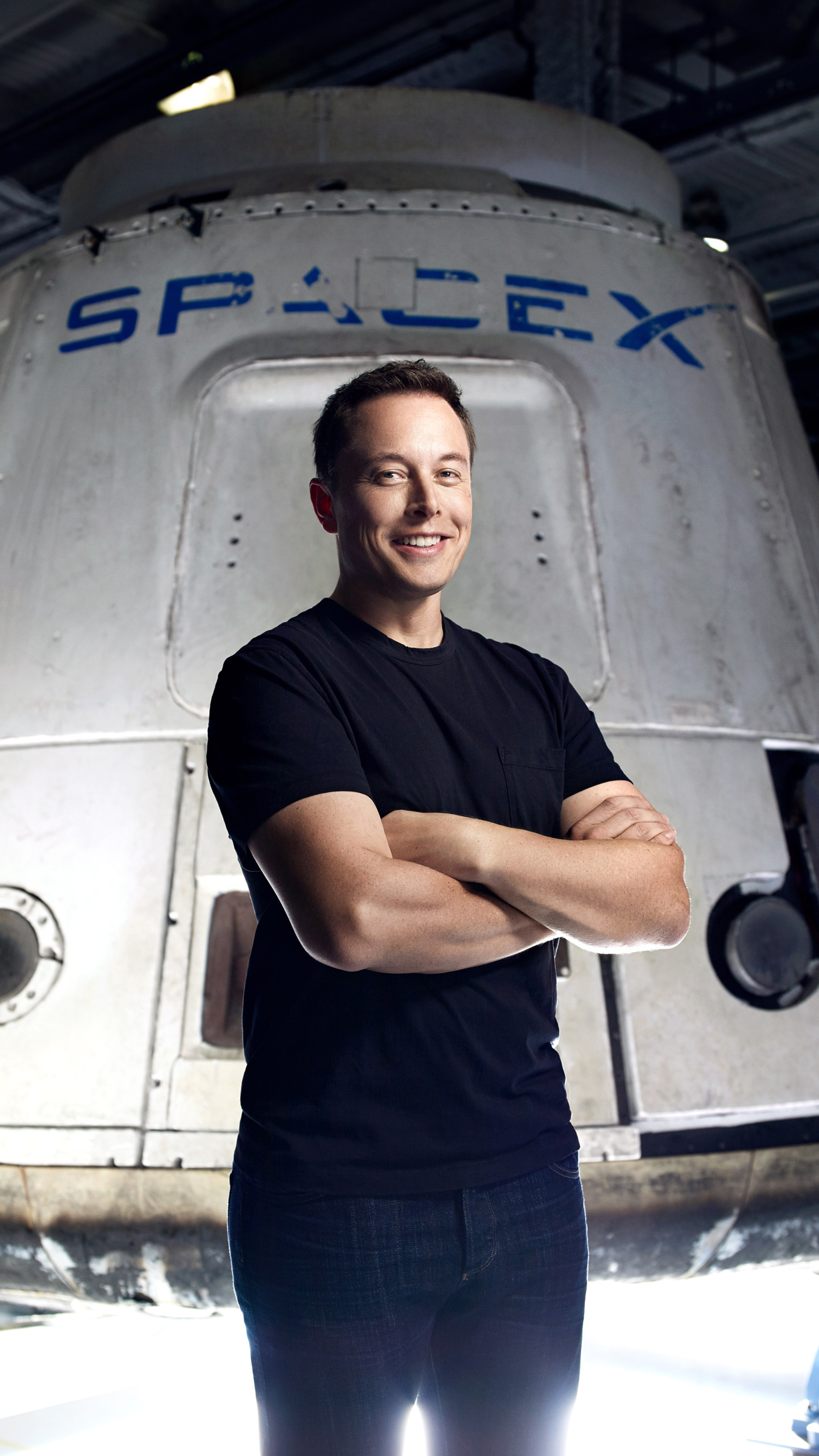 Elon Musk, CEO of SpaceX, stands with his arms crossed in front of a SpaceX spacecraft