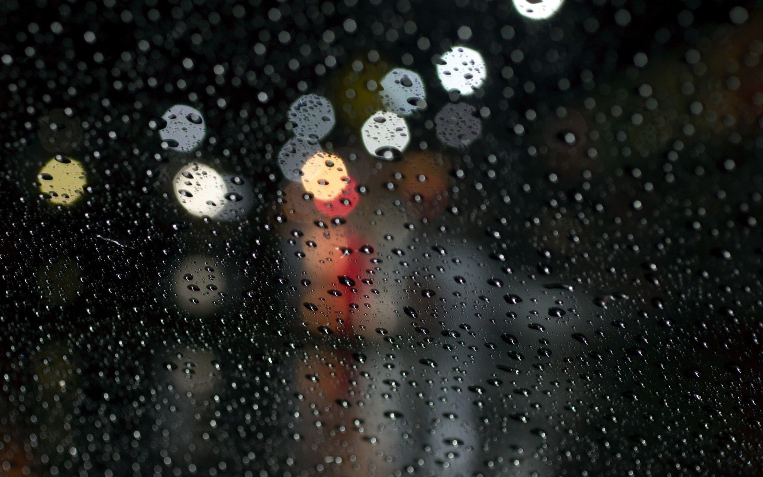 Raindrops on a window pane at night, with blurred city lights in the background