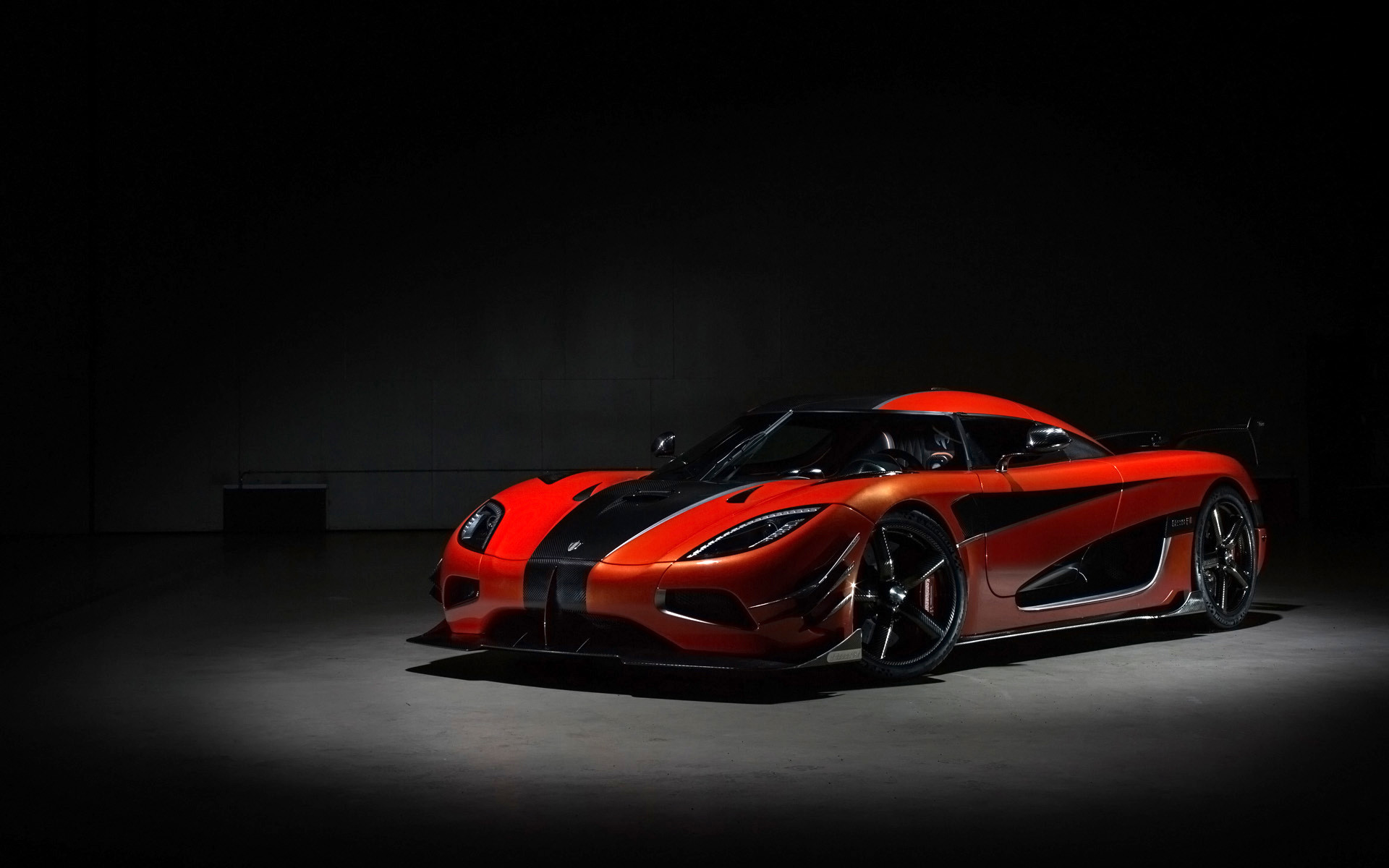 A sleek, red and black Koenigsegg sports car in a dark studio setting
