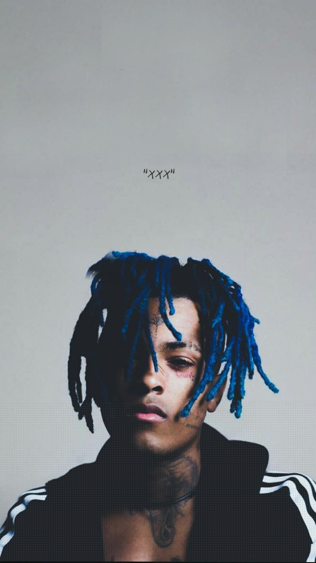 Close-up portrait of XXXTentacion with blue dreadlocks, showcasing his distinctive facial tattoos and intense gaze