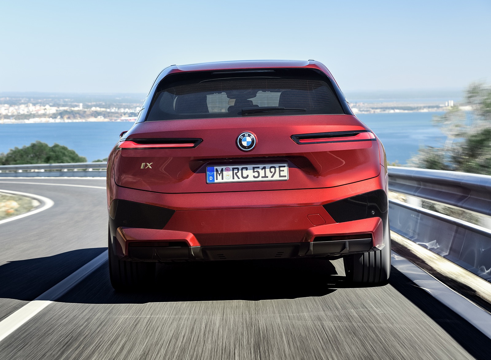 Rear view of a red BMW iX driving on a coastal highway