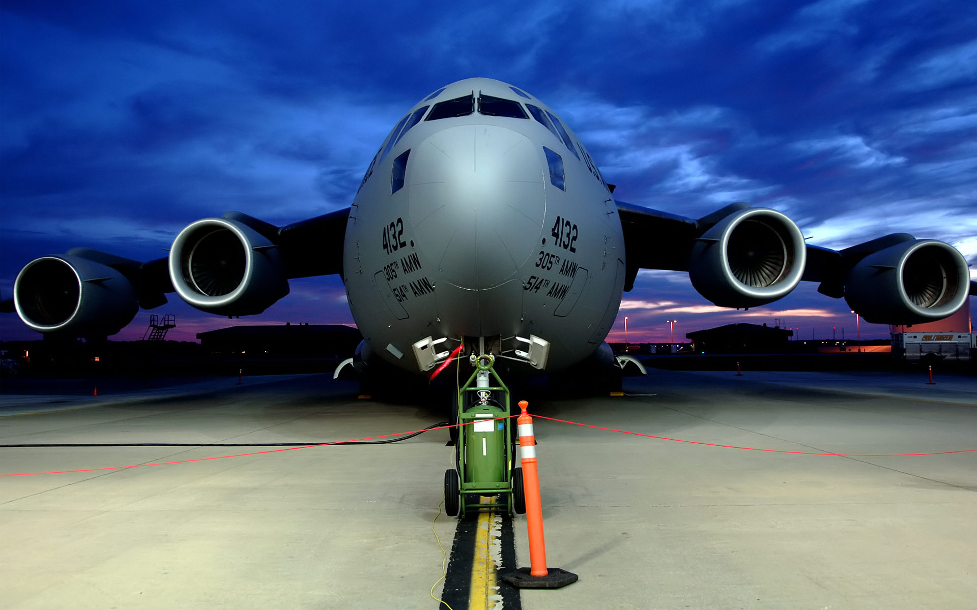 A C-17 Globemaster III military transport aircraft parked on the tarmac at dusk, its powerful engines and imposing size dominating the scene