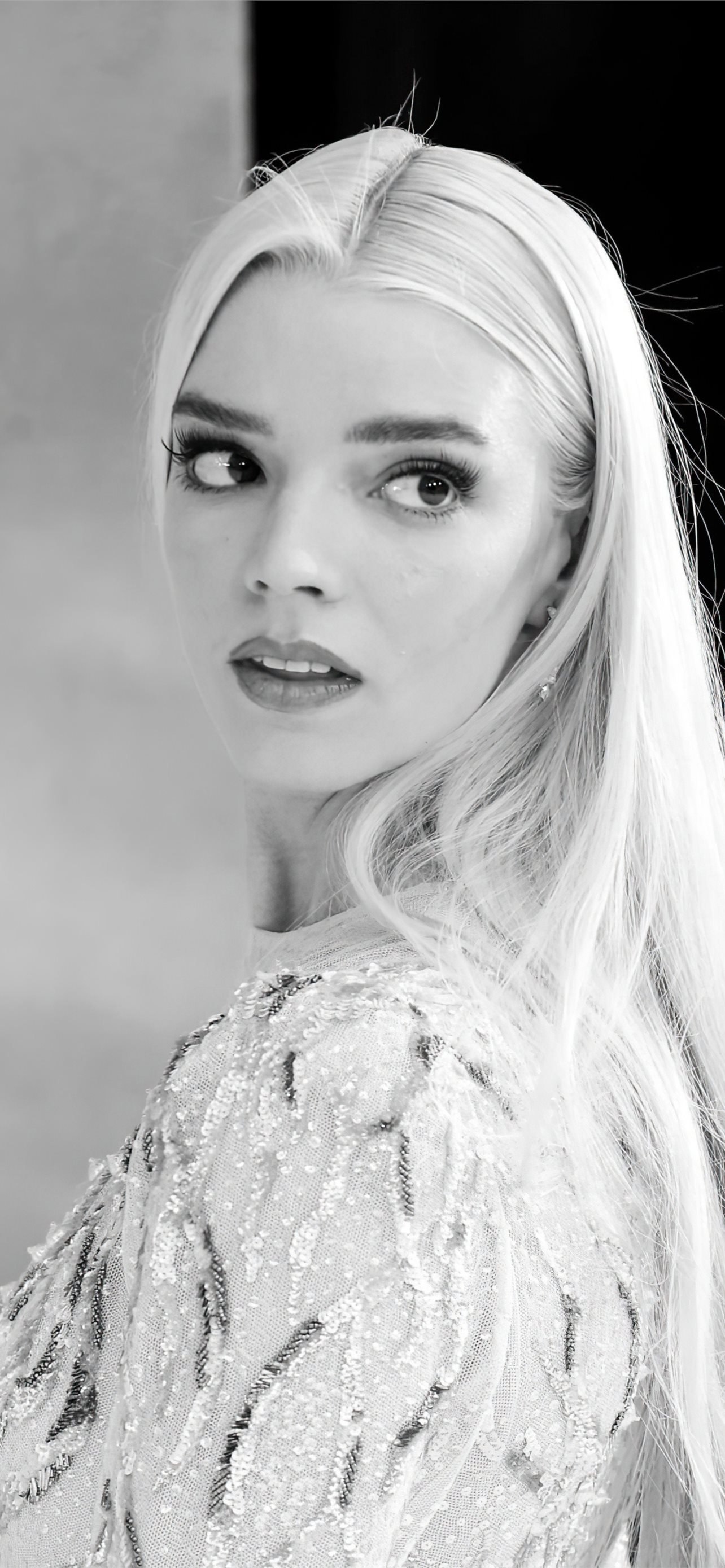 Black and white portrait of Anya Taylor-Joy, featuring her looking over her shoulder. She wears a sheer, embellished top
