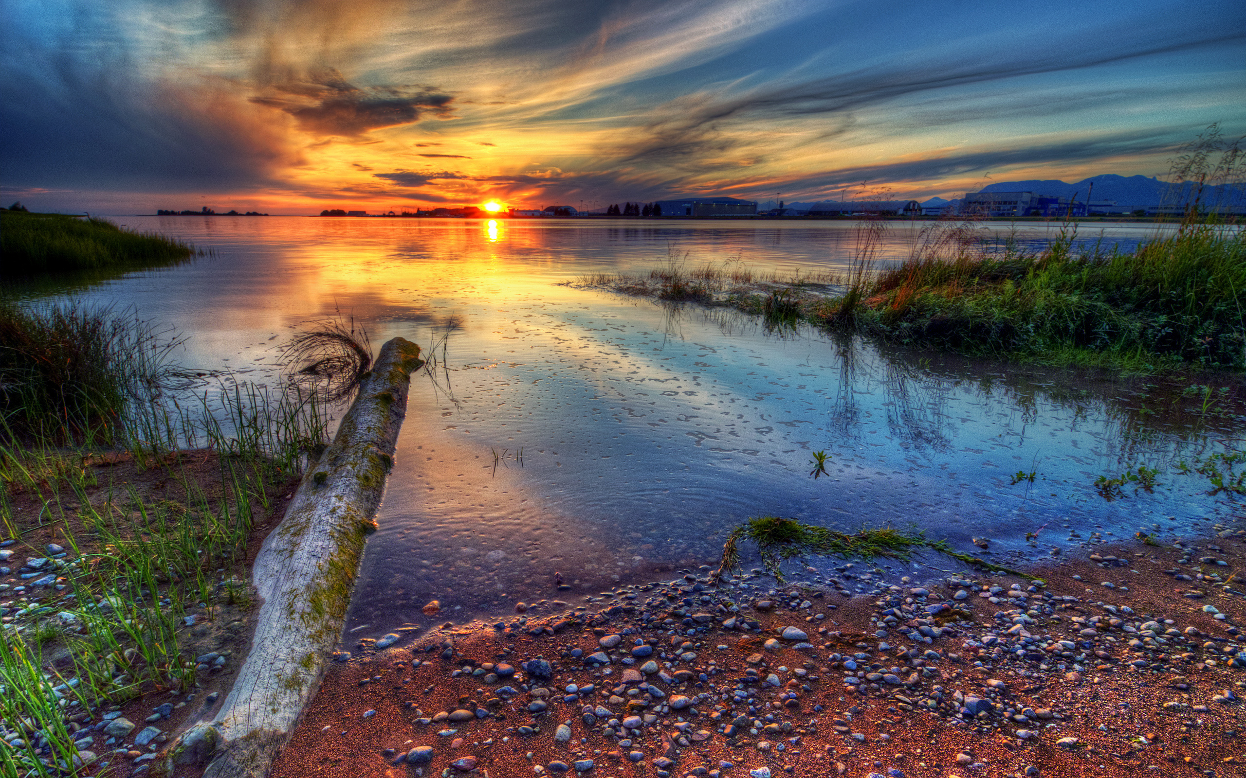 A breathtaking sunset over a tranquil lake, with the colorful sky reflected in the water and a weathered log in the foreground