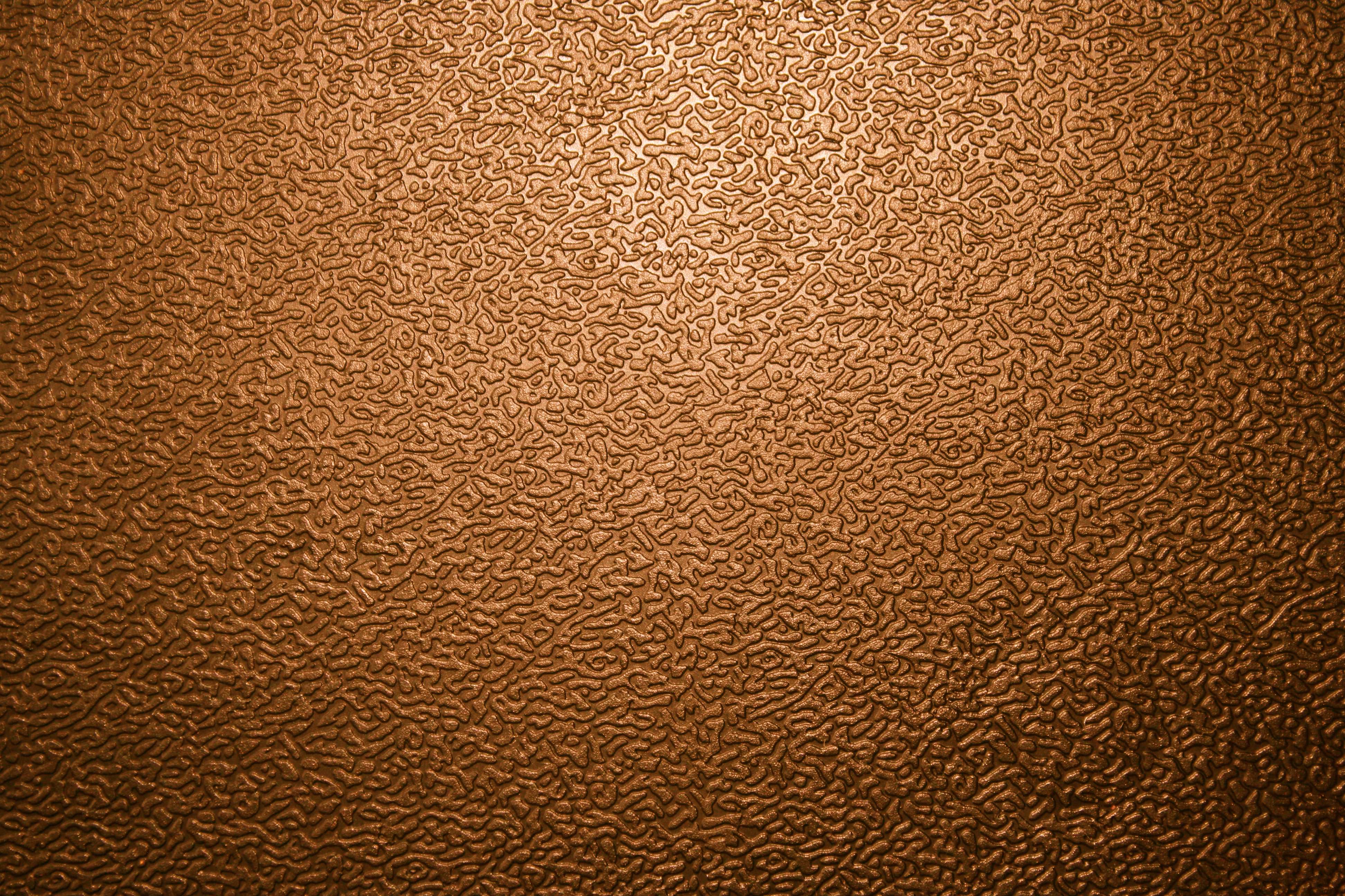Close-up of a textured brown surface, resembling hammered metal or patterned plastic, with subtle light reflections highlighting the intricate details