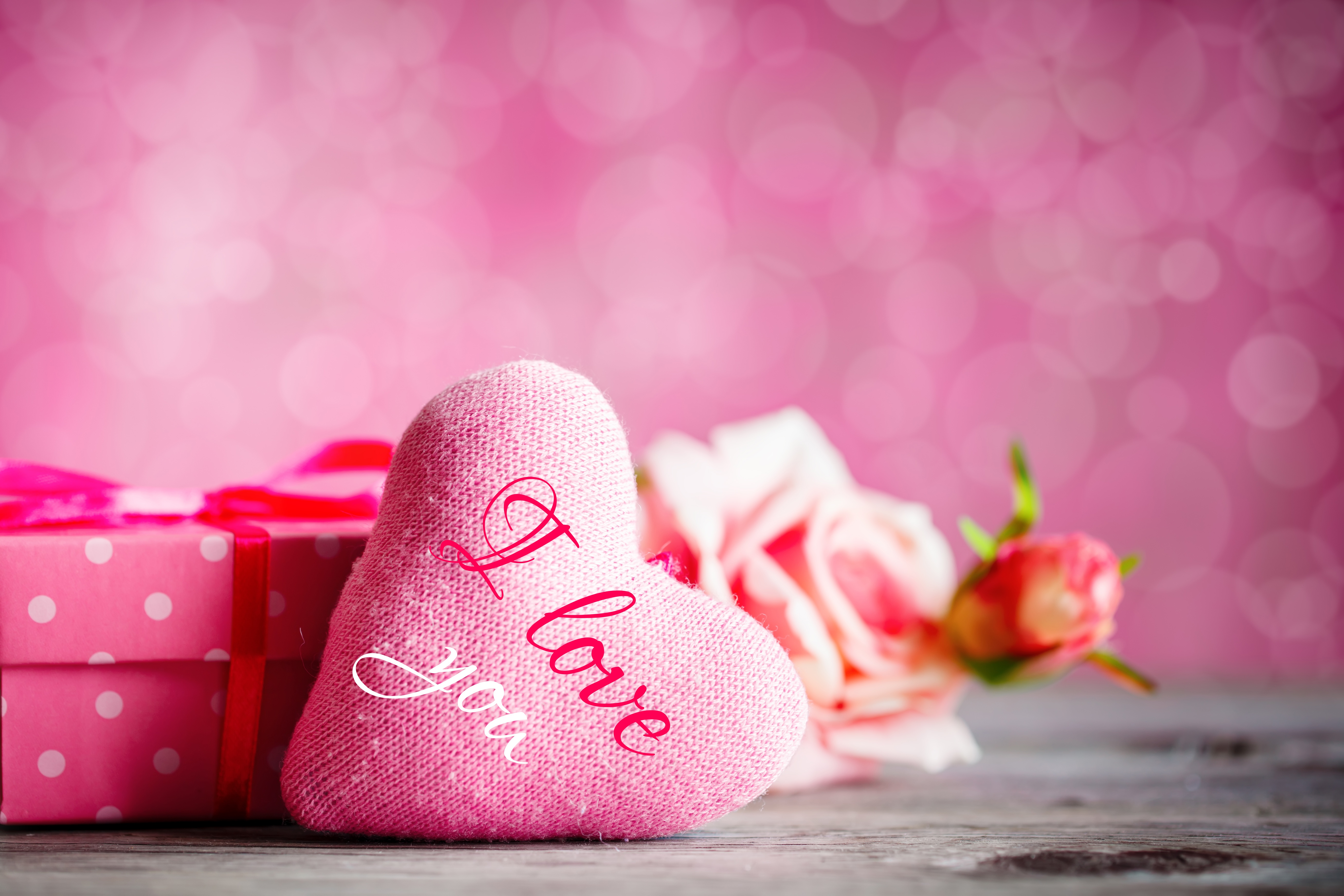Valentine's Day still life with pink heart, gift box, and roses on a wooden surface with a bokeh background