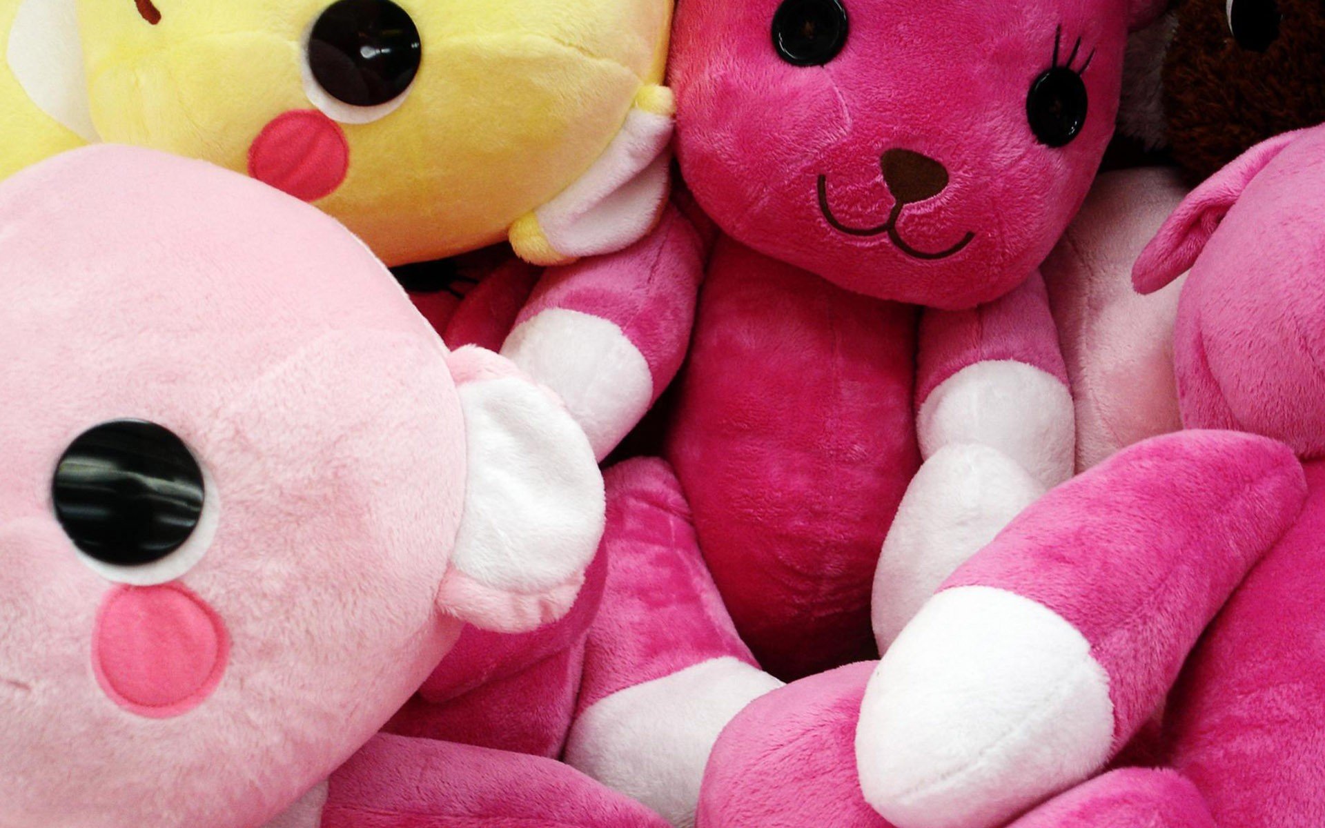 Close-up of a pile of colorful plush toys, featuring various characters and bright pink, yellow, and white colors