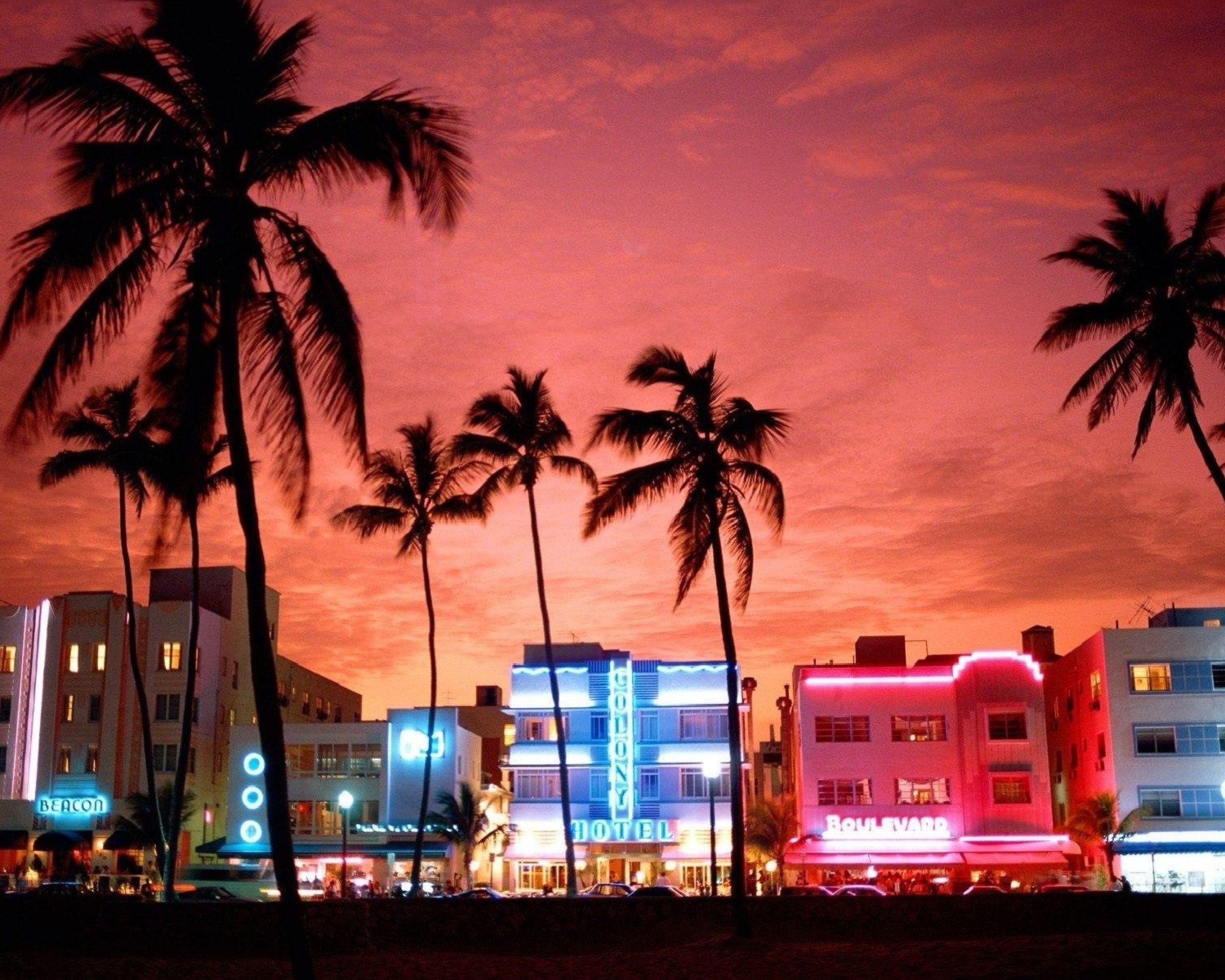 Silhouetted palm trees against a vibrant sunset in Miami Beach, with neon-lit Art Deco hotels in the foreground