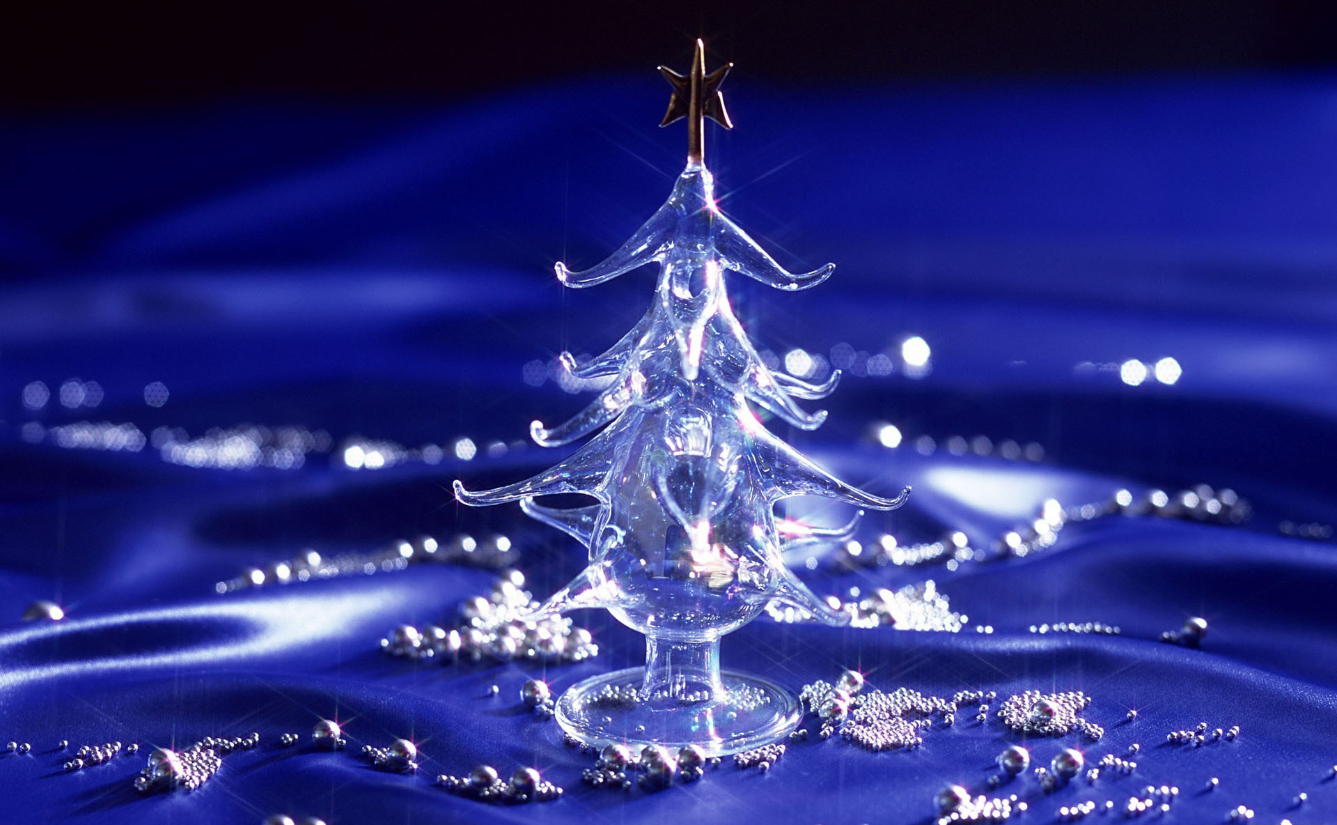 Elegant glass Christmas tree on a blue satin background with silver beads