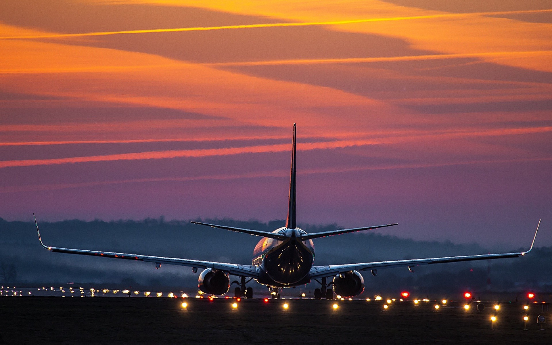 A passenger airplane silhouetted against a vibrant sunset on the airport runway