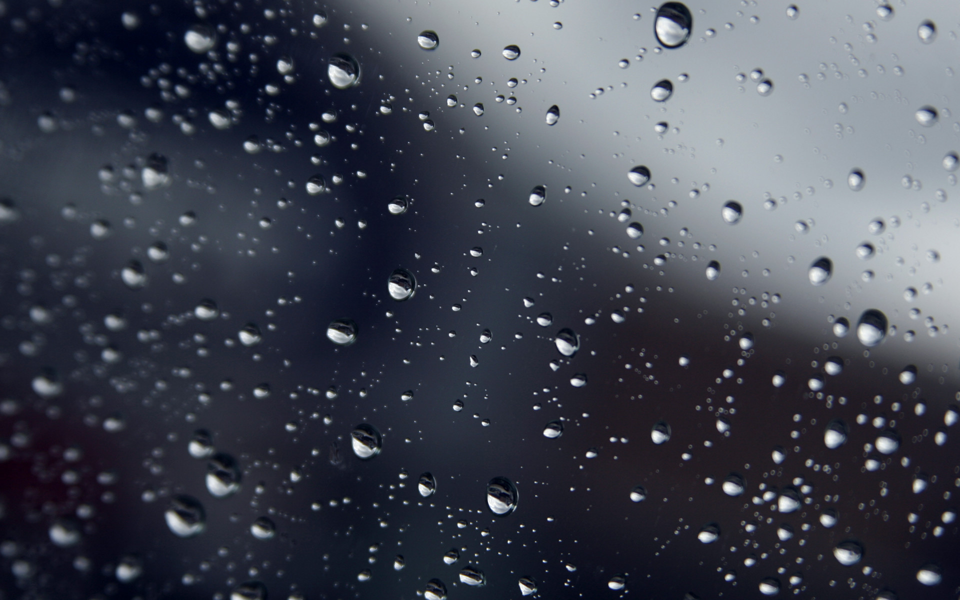 Close-up of raindrops on a window against a blurred background, creating a textured and abstract pattern