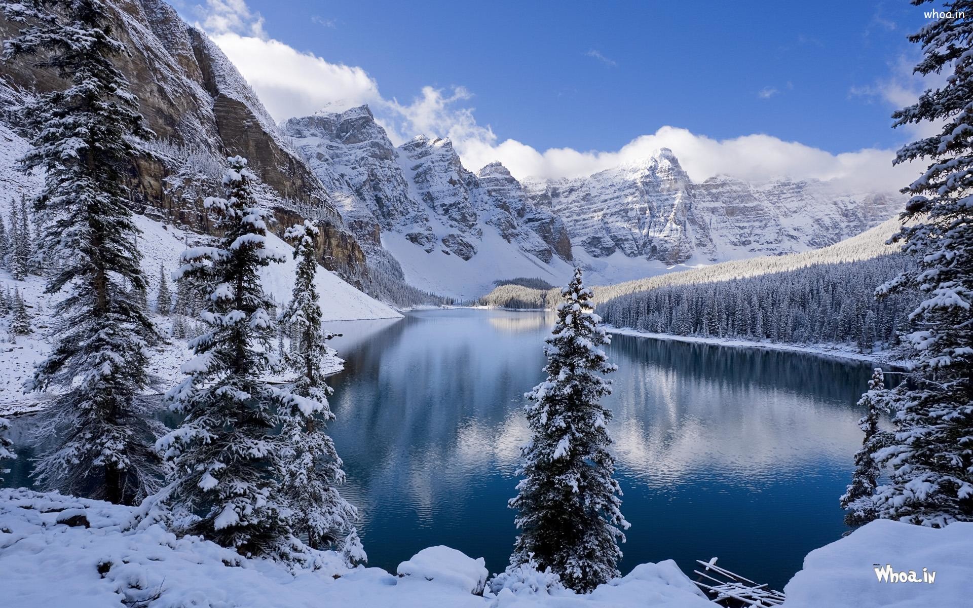 Serene winter landscape with snow-covered mountains and a pristine lake reflecting a clear blue sky