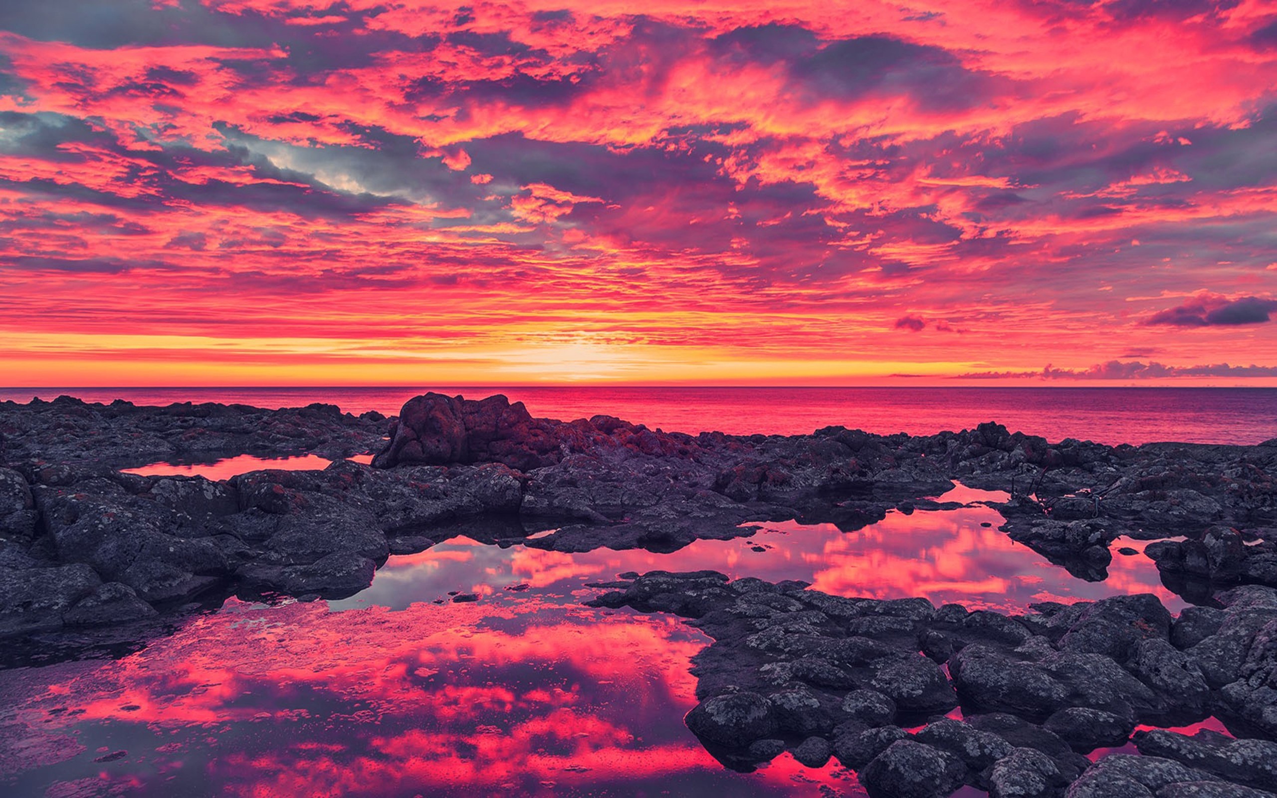 Vivid pink and orange sunset reflected in tide pools on a rocky beach