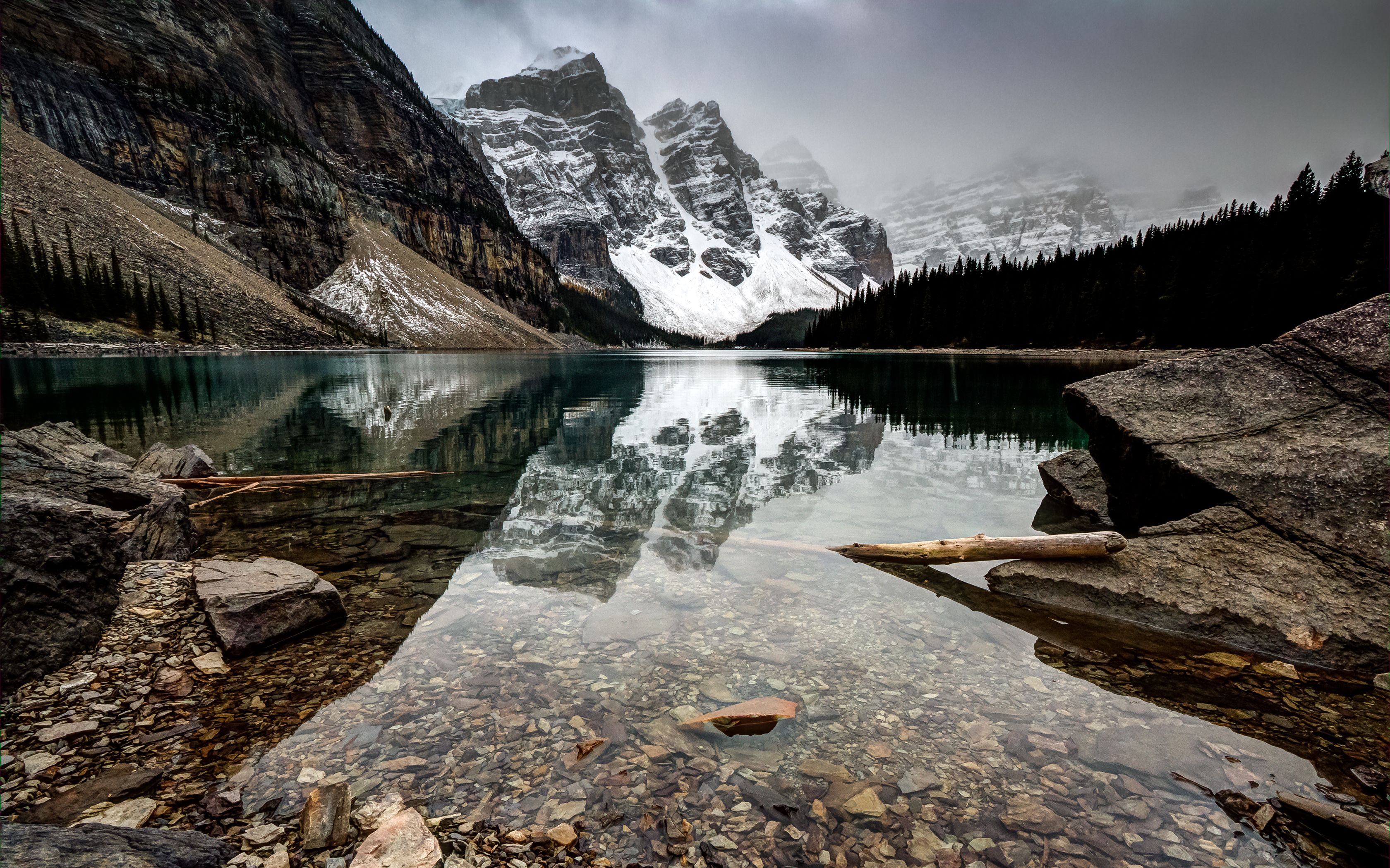 Stunning 4k wallpaper of a pristine alpine lake reflecting snow-capped mountains and a cloudy sky