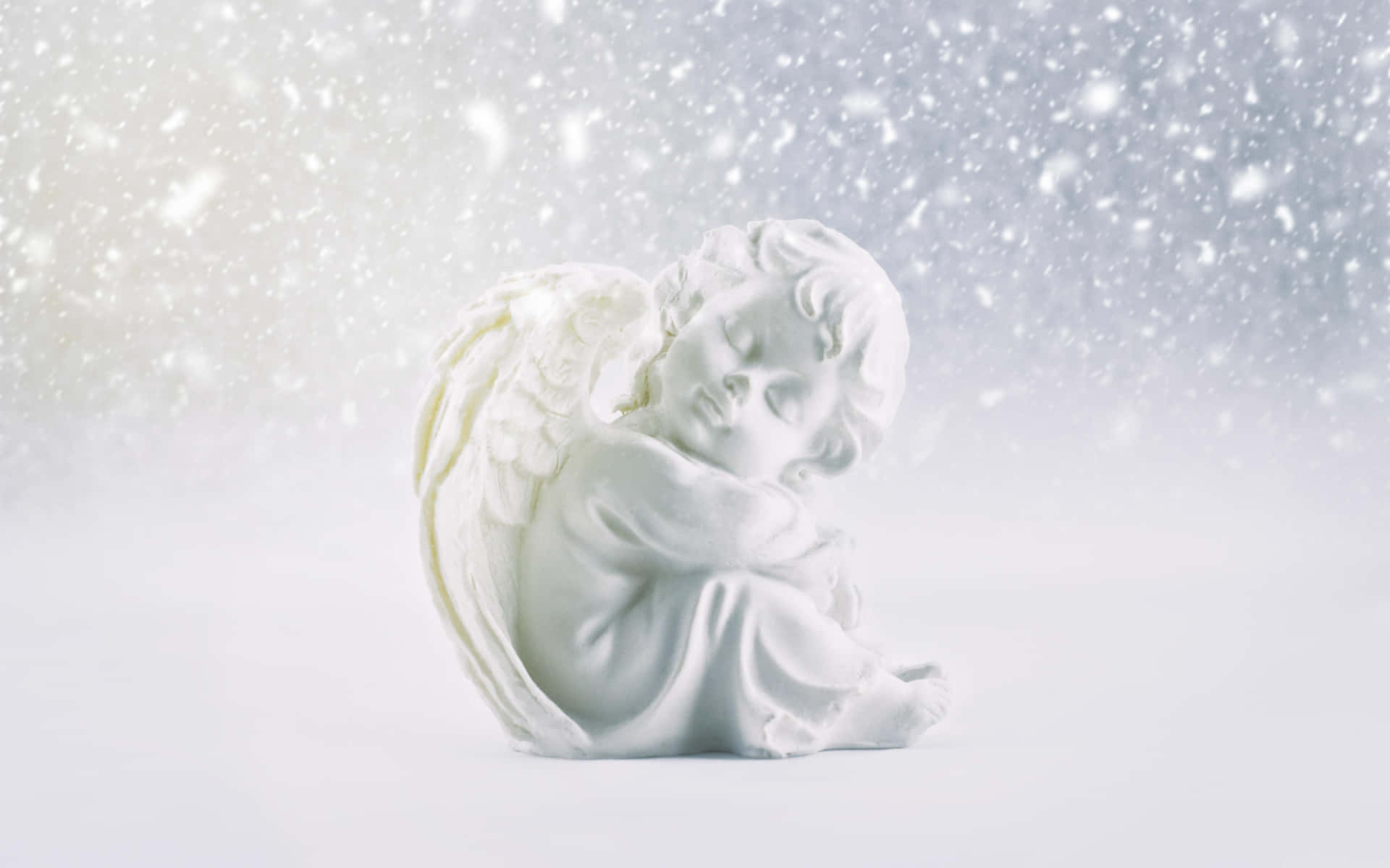 A serene white cherubic angel figurine sits peacefully amidst a gentle snowfall, evoking a sense of tranquility and winter wonder