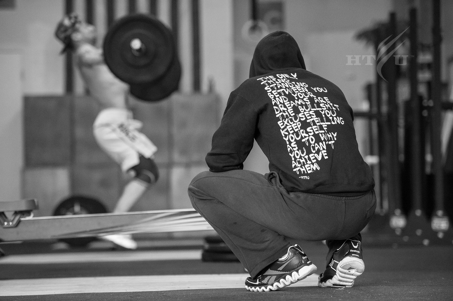 A Crossfit athlete performing a snatch lift with a barbell, while another person observes