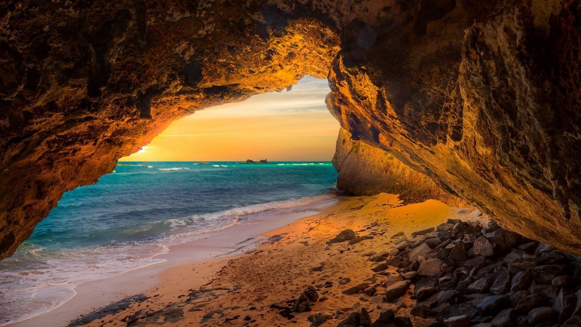 Sunset view from inside a sea cave, with golden sand and turquoise water