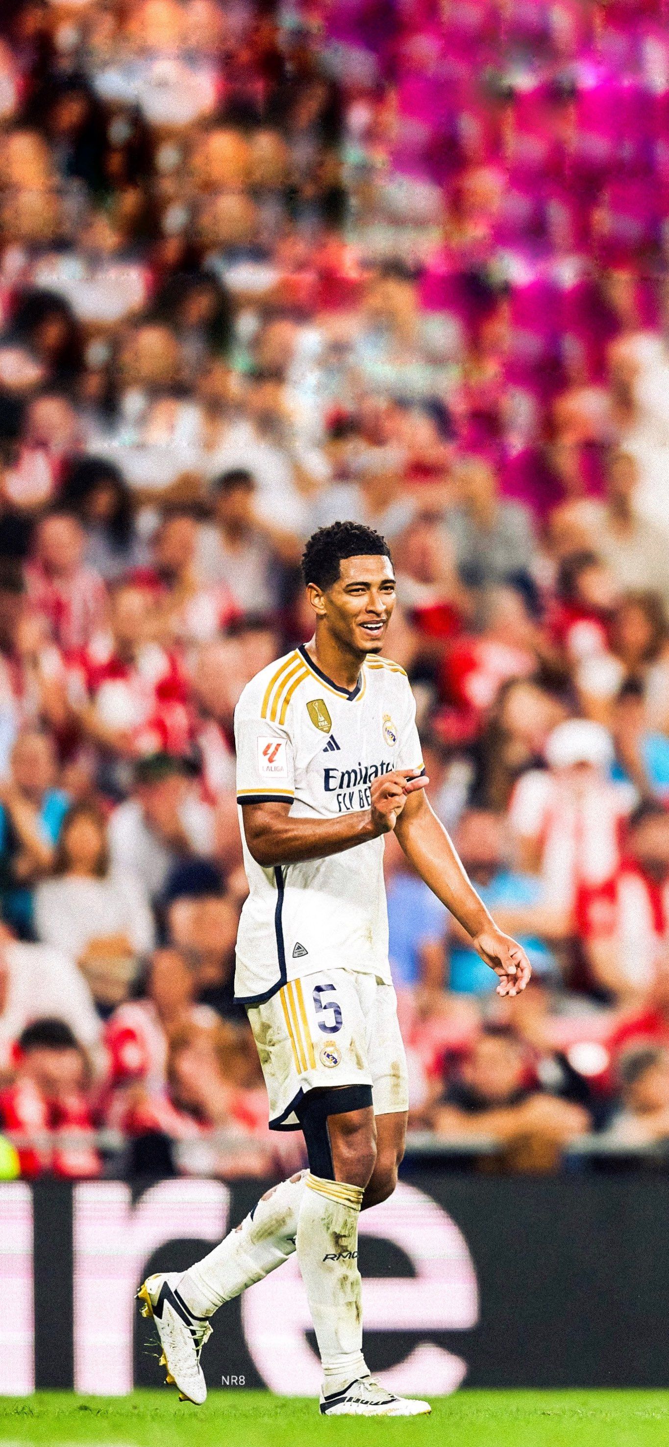 Jude Bellingham in action during a Real Madrid match. He is wearing the team's white and gold kit and his expression suggests focus and determination