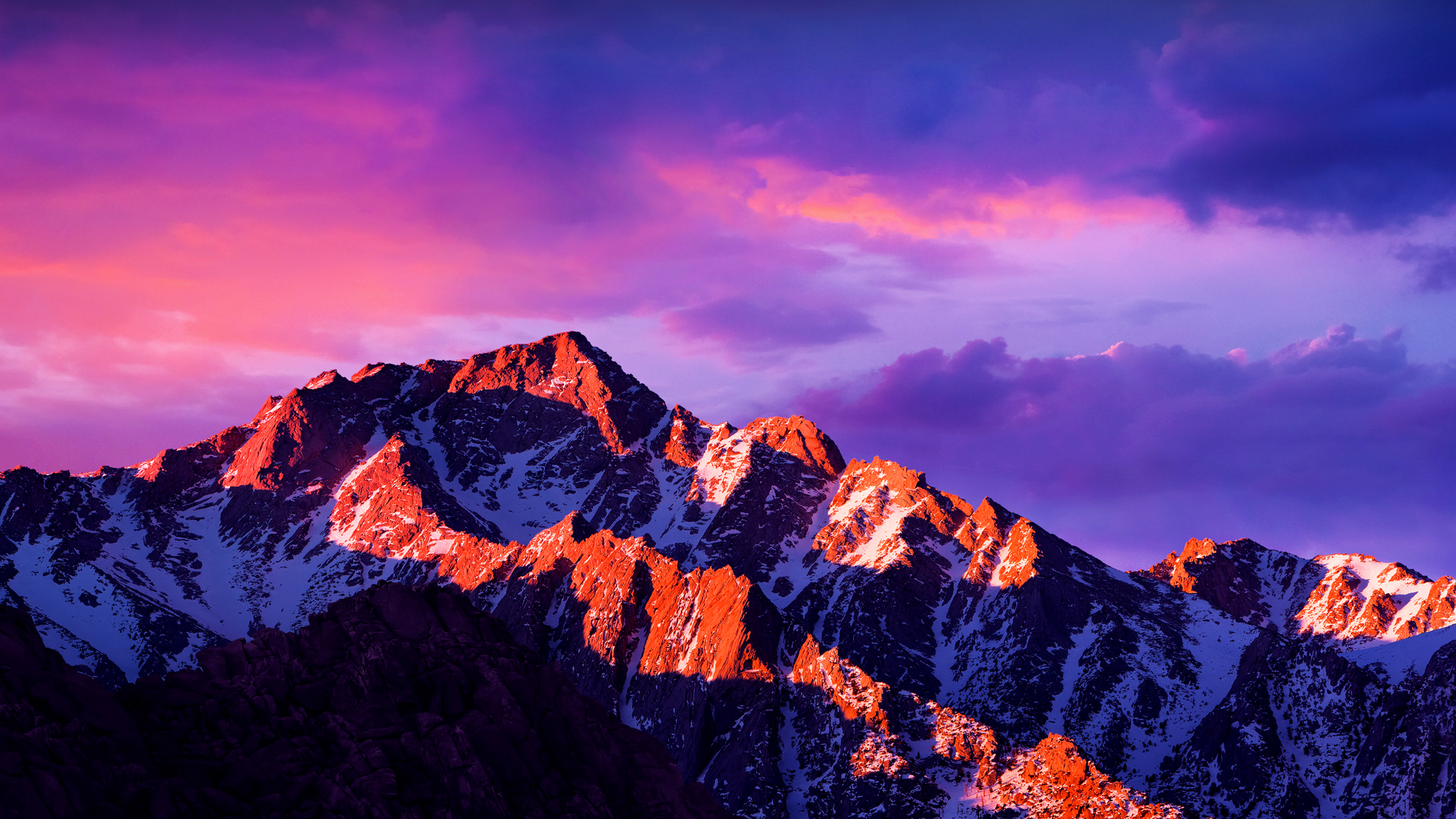 Majestic snow-capped mountain range at sunset, bathed in vibrant pink and purple hues - perfect for a MacBook wallpaper
