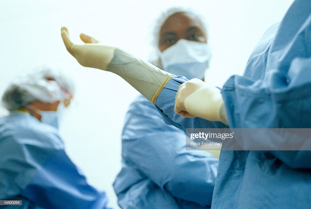 Surgeon Putting On Gloves Surgery Staff In Background Stock Photo