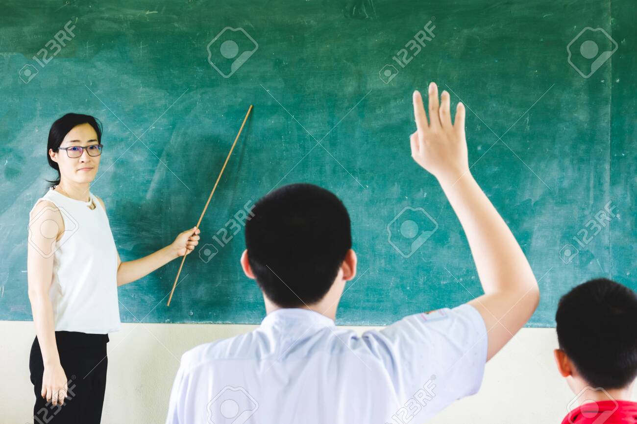 Asian Teacher Teaching In Classroom With Cholkboard Background