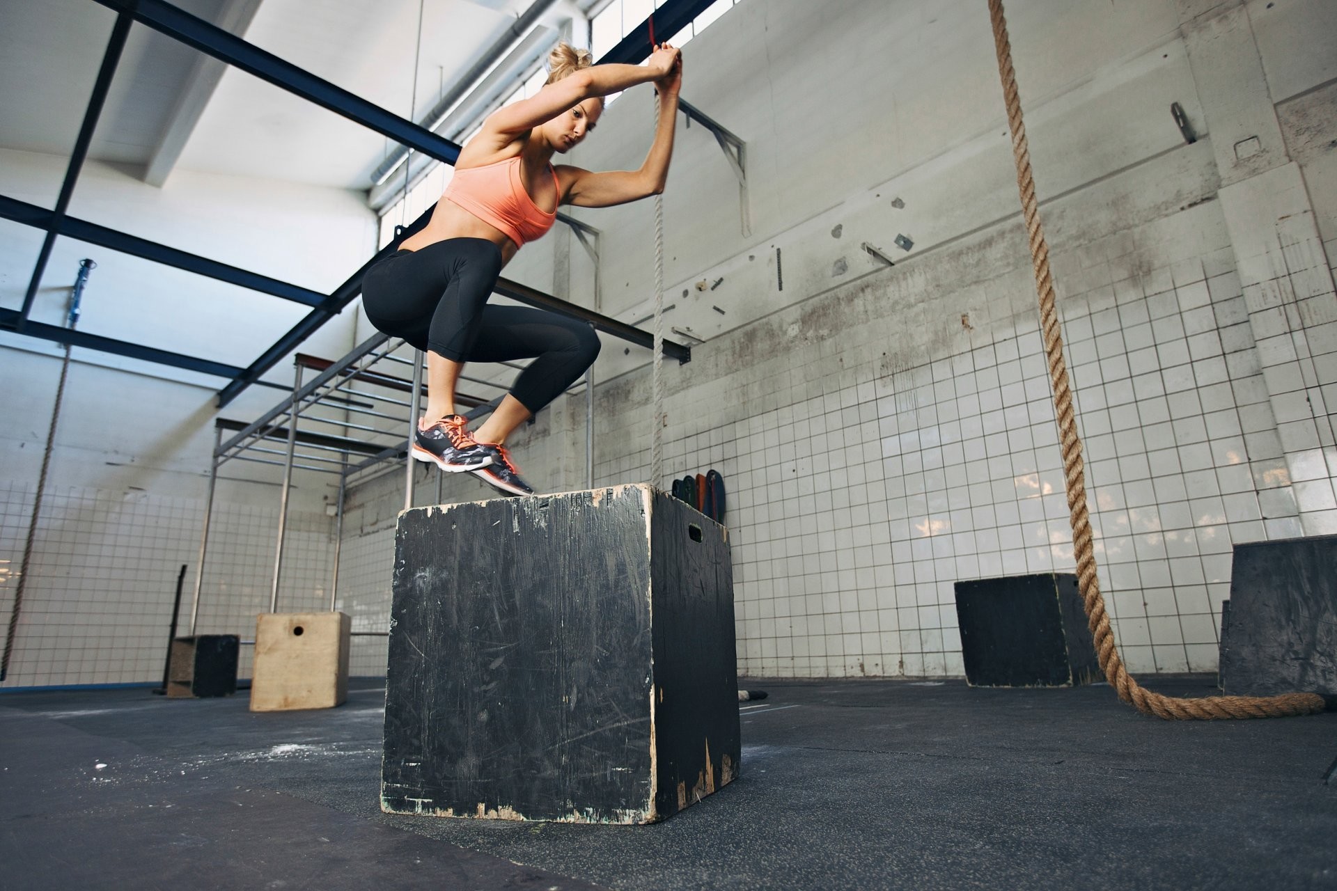A woman performing a box jump in a CrossFit gym, demonstrating strength and athleticism