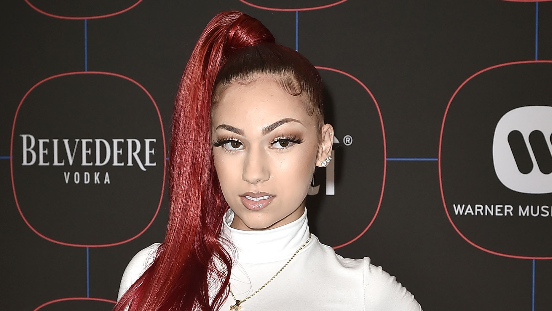 Bhad Bhabie at a Warner Music event, posing against a backdrop with brand logos