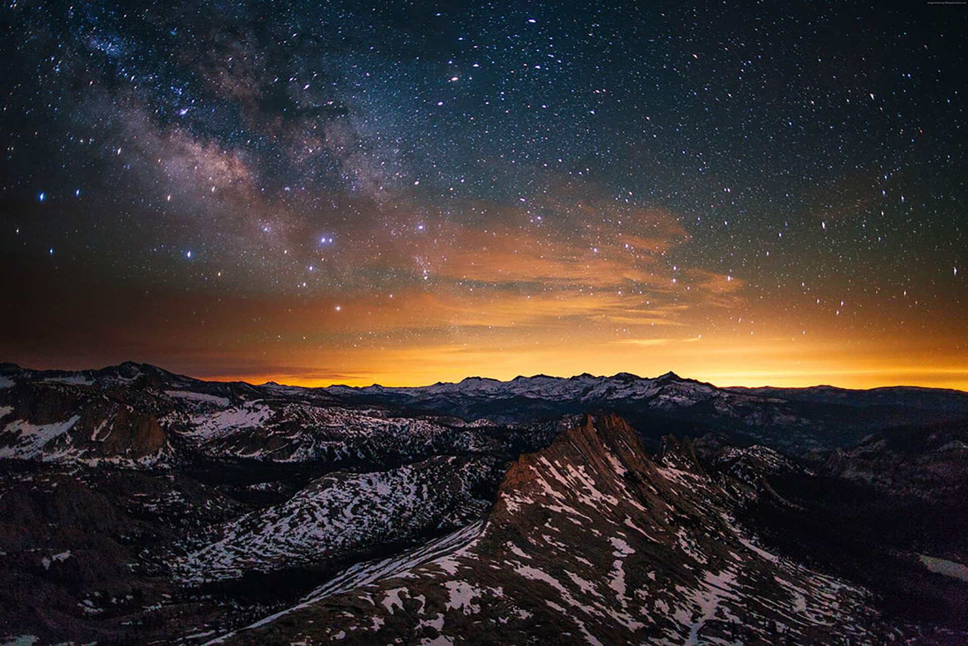 A breathtaking vista of a snow-capped mountain range under a vibrant Milky Way galaxy, with the warm hues of sunset illuminating the horizon