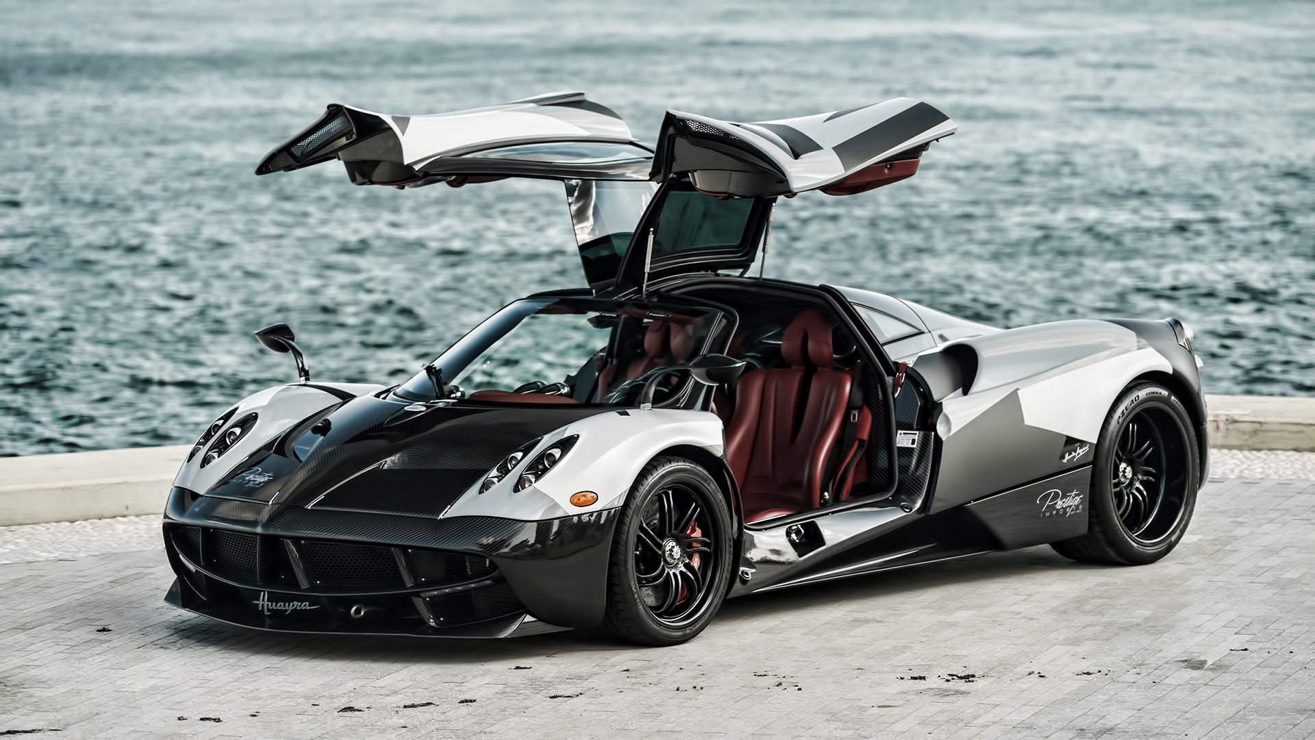 A stunning Pagani Huayra supercar with its distinctive gull-wing doors open, parked by the water