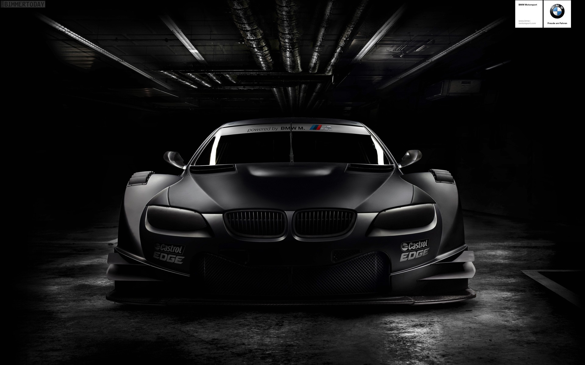A sleek, black BMW race car parked in a dimly lit garage, showcasing its aggressive body kit and motorsport-inspired design