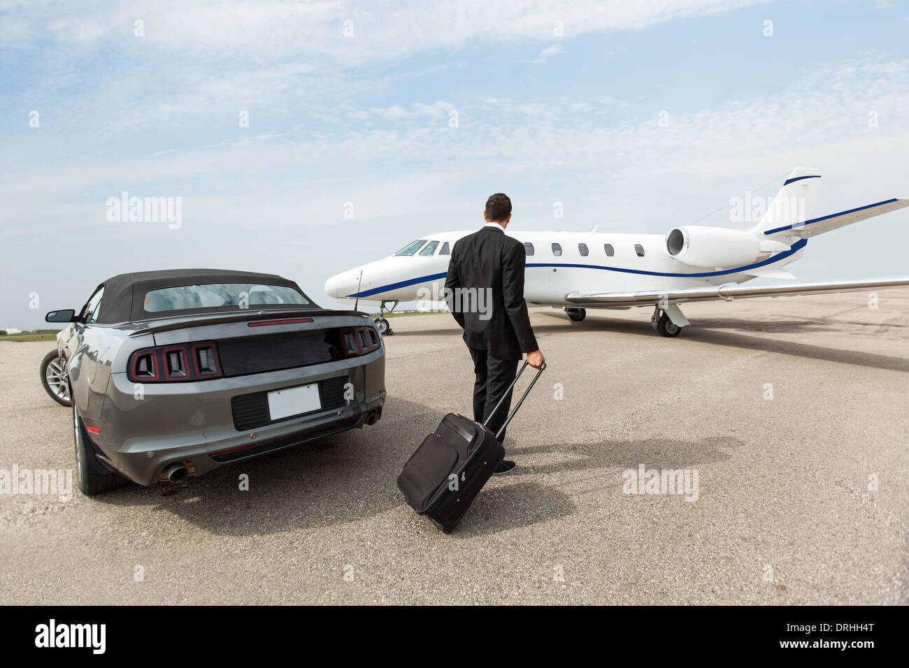 Businessman Standing By Car And Private Jet At Terminal Stock