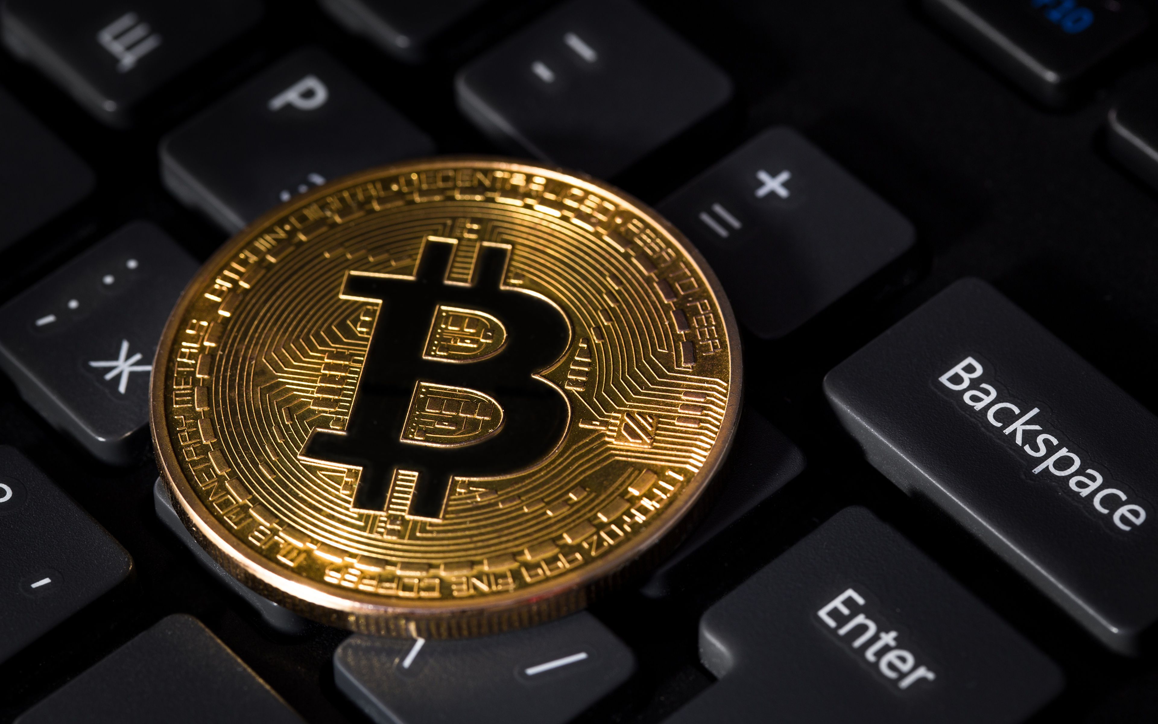 Gold Bitcoin coin resting on a black computer keyboard, signifying the intersection of cryptocurrency and technology
