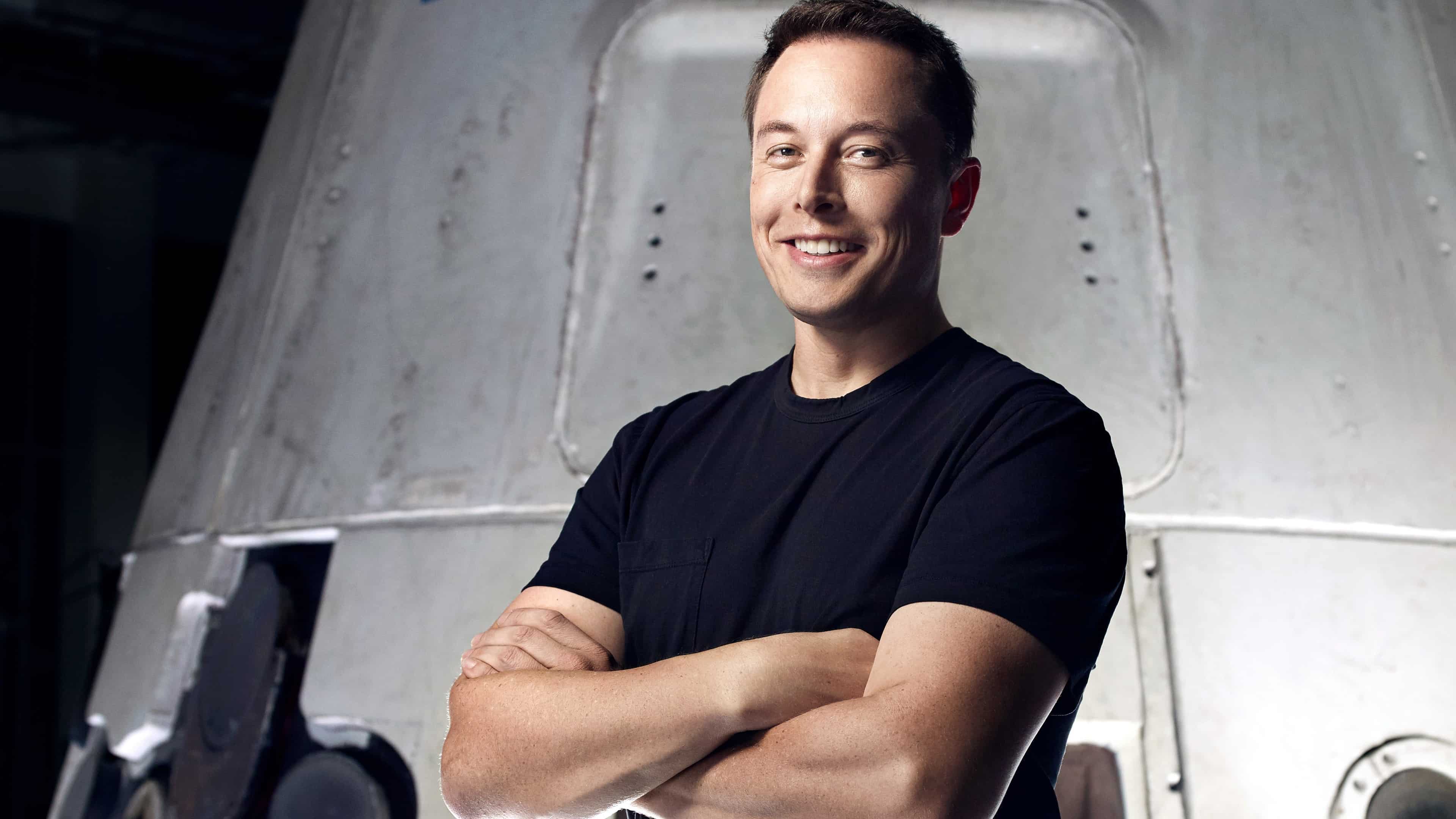 Elon Musk, CEO of SpaceX and Tesla, stands with his arms crossed in front of a SpaceX spacecraft