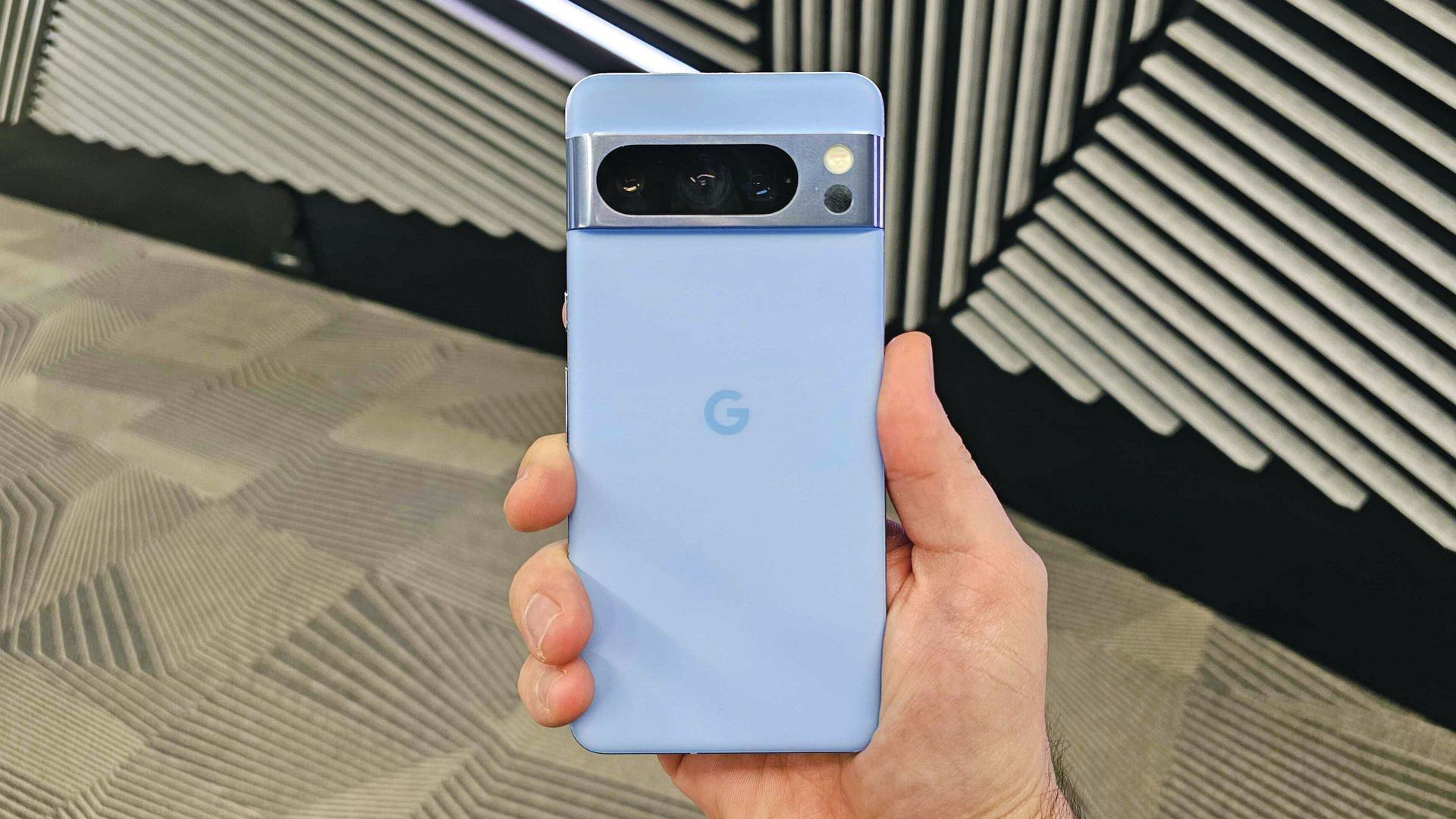 A hand holding a light blue Google Pixel phone with a prominent camera bar