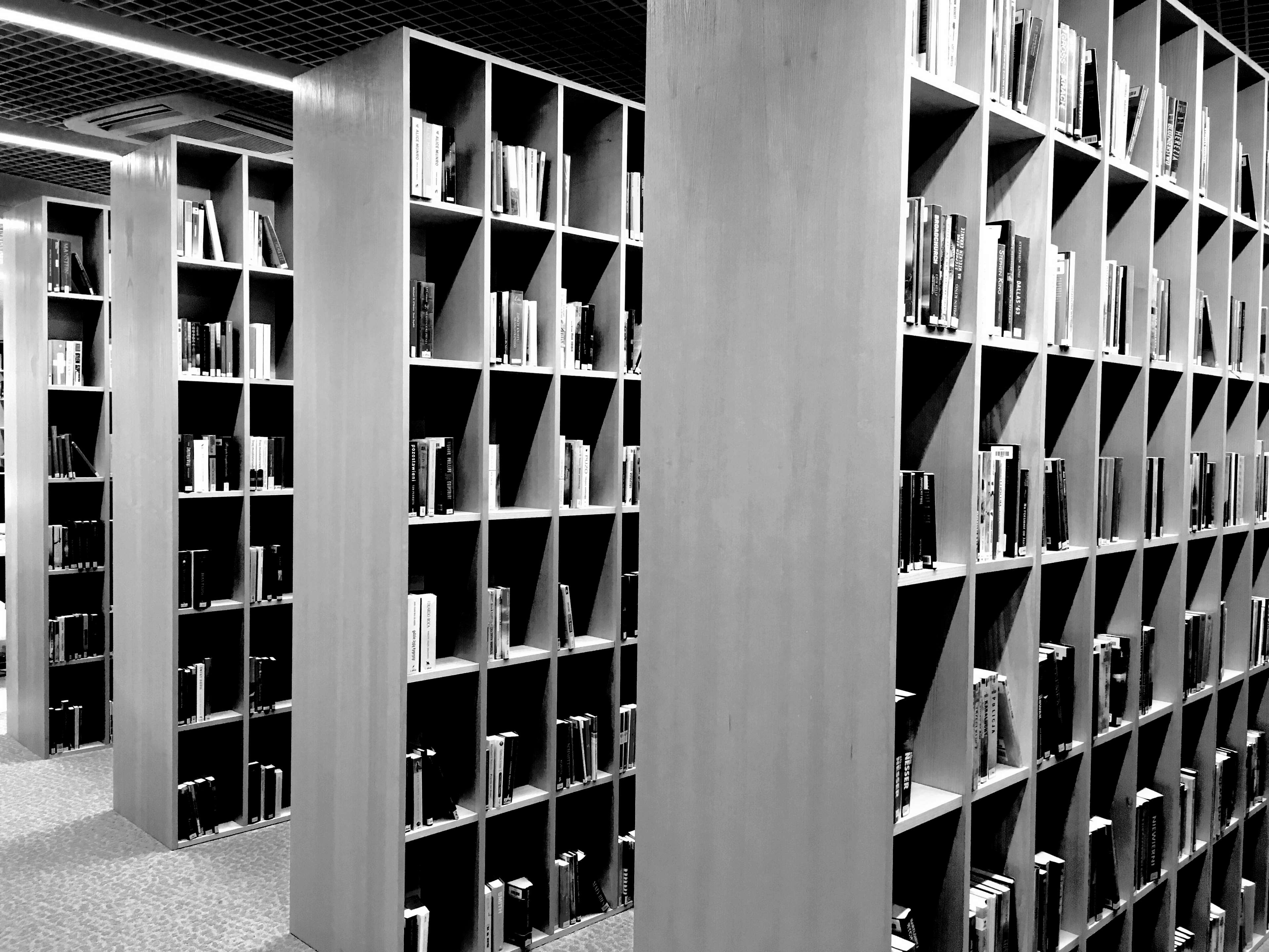 A grayscale photograph of a modern library, featuring tall, sleek bookshelves filled with various books. The image highlights the organized and minimalist design of the space