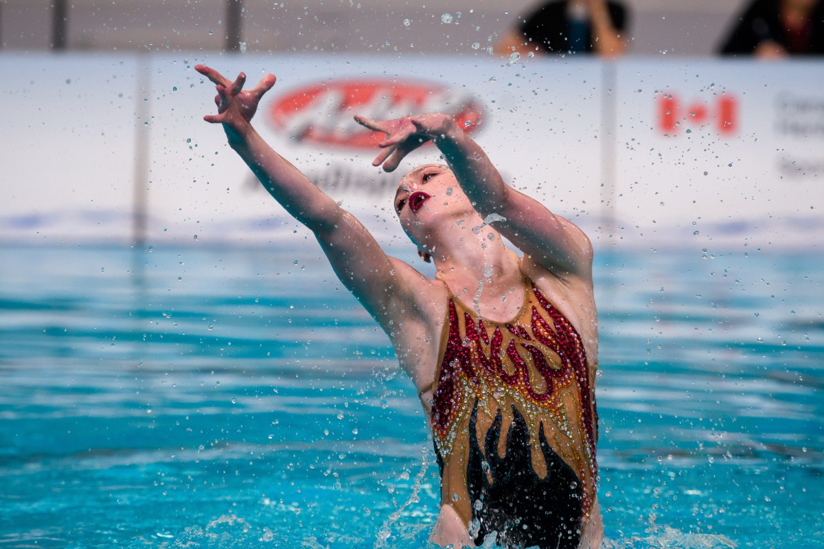 A female artistic swimmer performing a dramatic pose in a pool during a competition