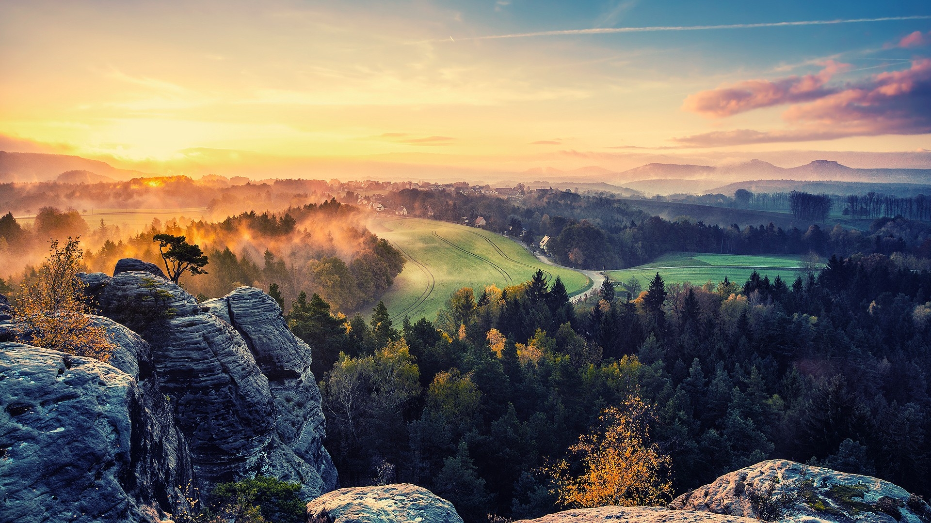 Sunrise over a picturesque valley with rolling hills, lush forests, and a rocky cliff in the foreground
