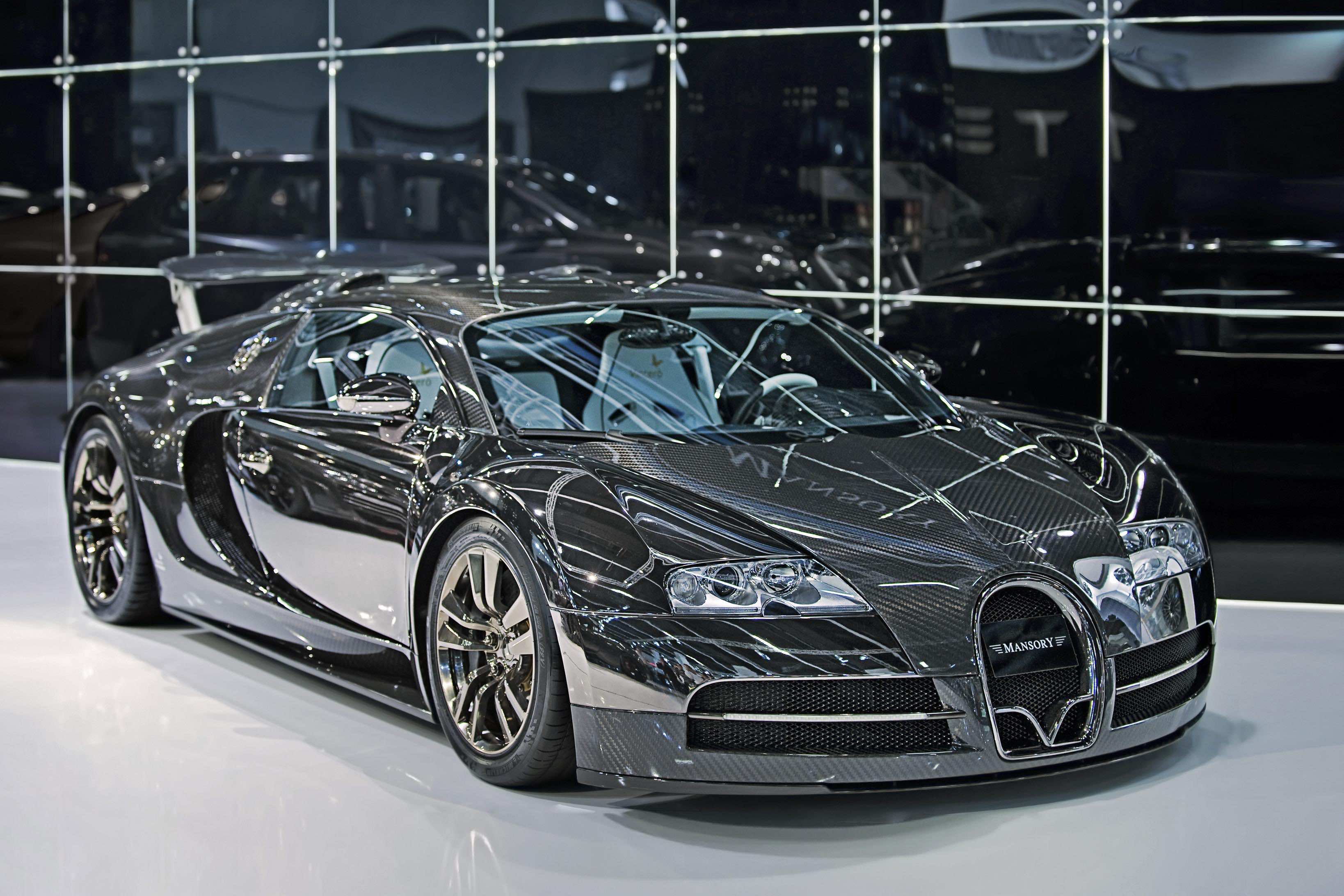 A sleek, black Bugatti Veyron with visible carbon fiber bodywork. The car is displayed in an automotive showroom with reflective panels. The Bugatti logo is prominently visible on the front grill, indicating a high-performance, luxury vehicle