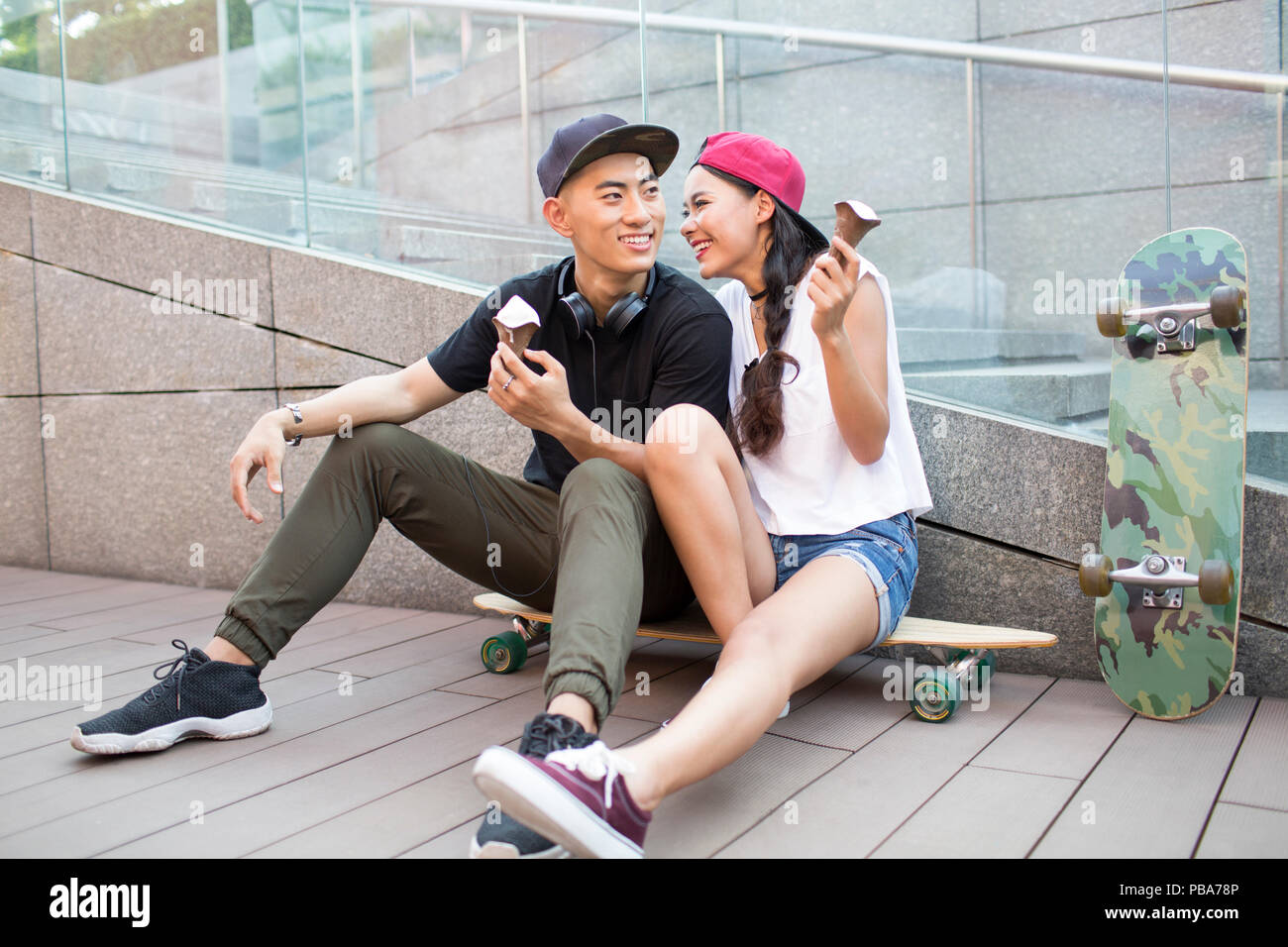 Cheerful young Chinese couple eating ice cream on skateboard Stock