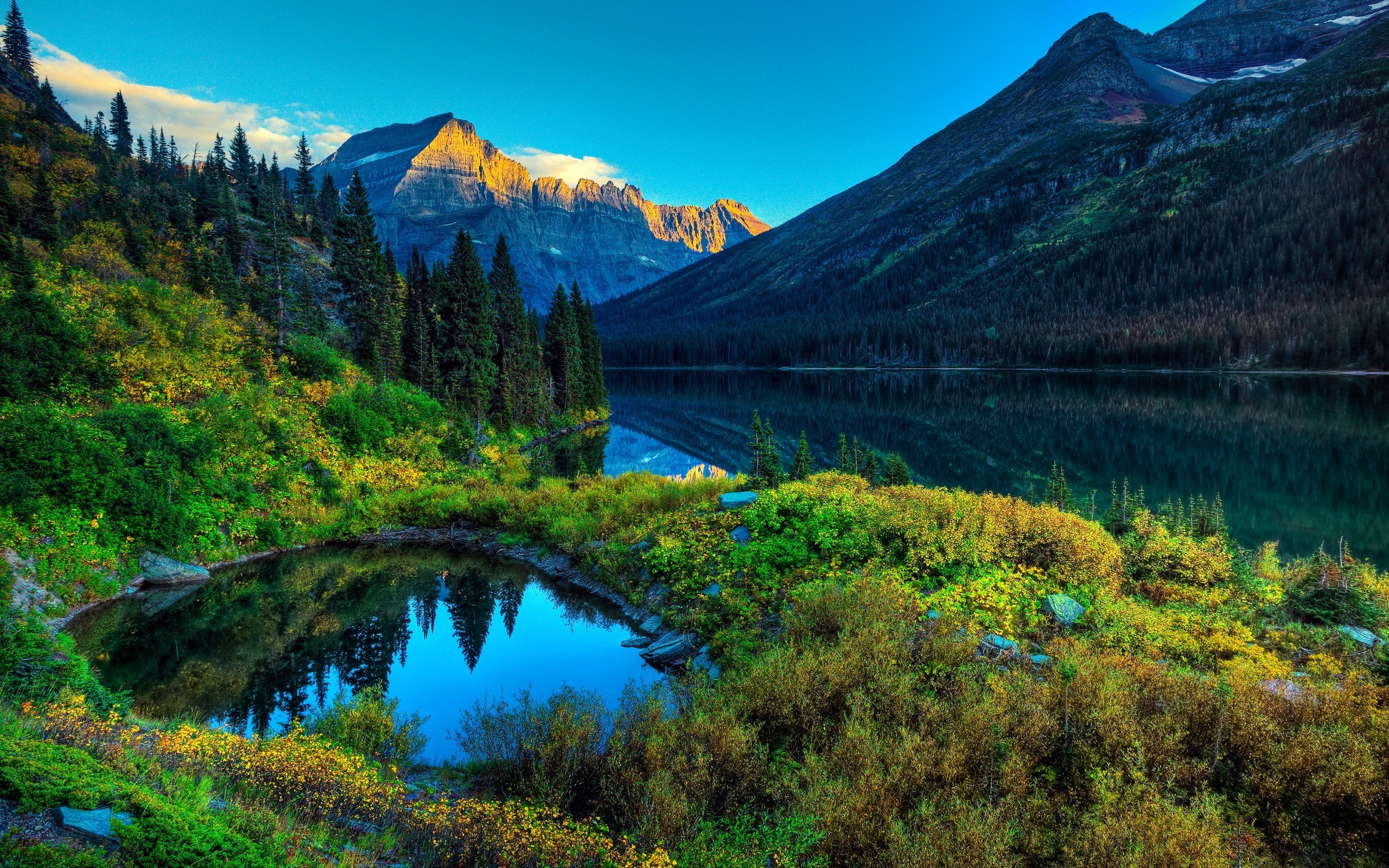 Stunning view of a crystal-clear alpine lake reflecting the surrounding mountains and lush greenery during sunset
