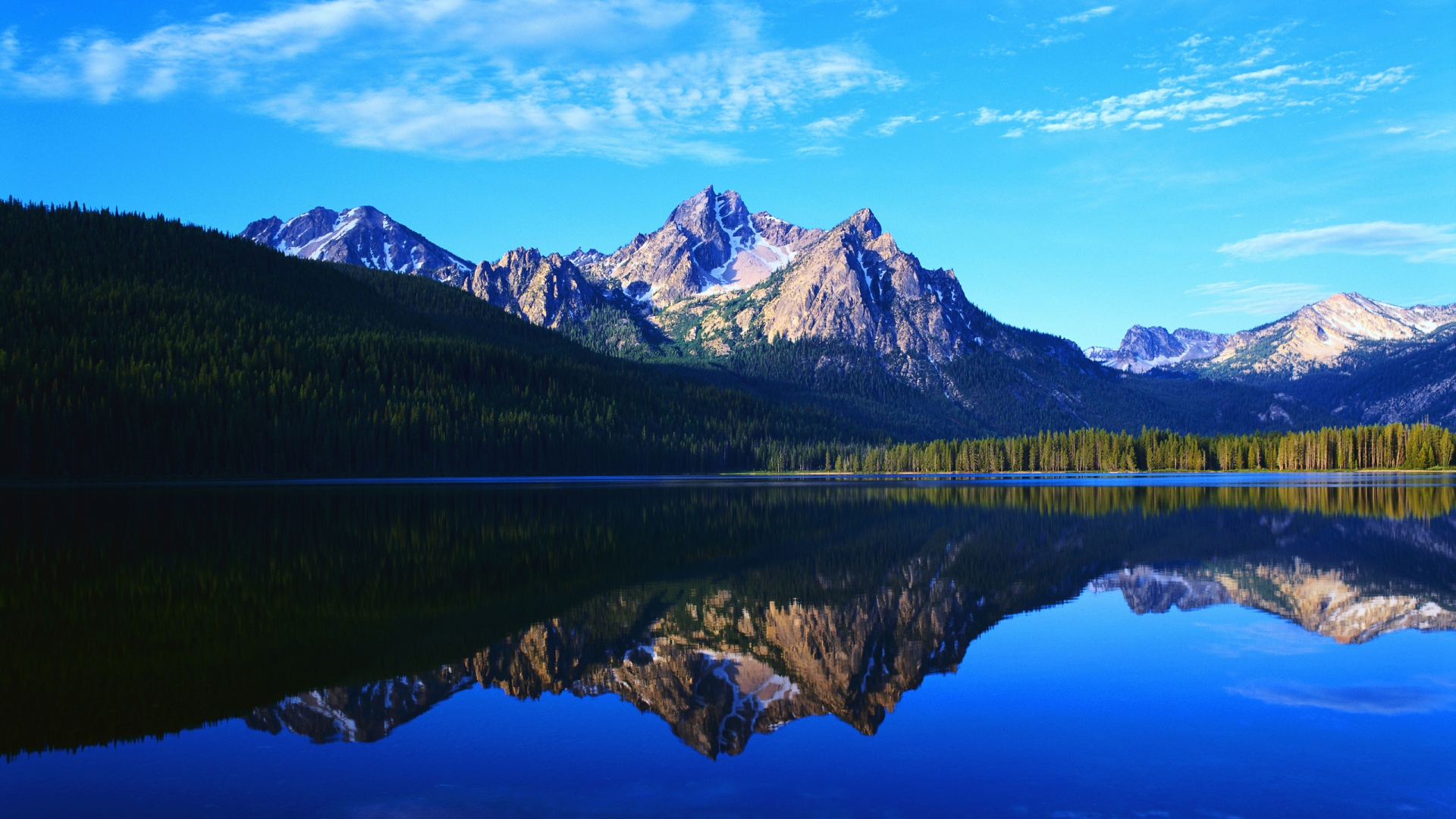 Serene mountain lake reflecting majestic peaks and a clear blue sky, perfect for a laptop wallpaper