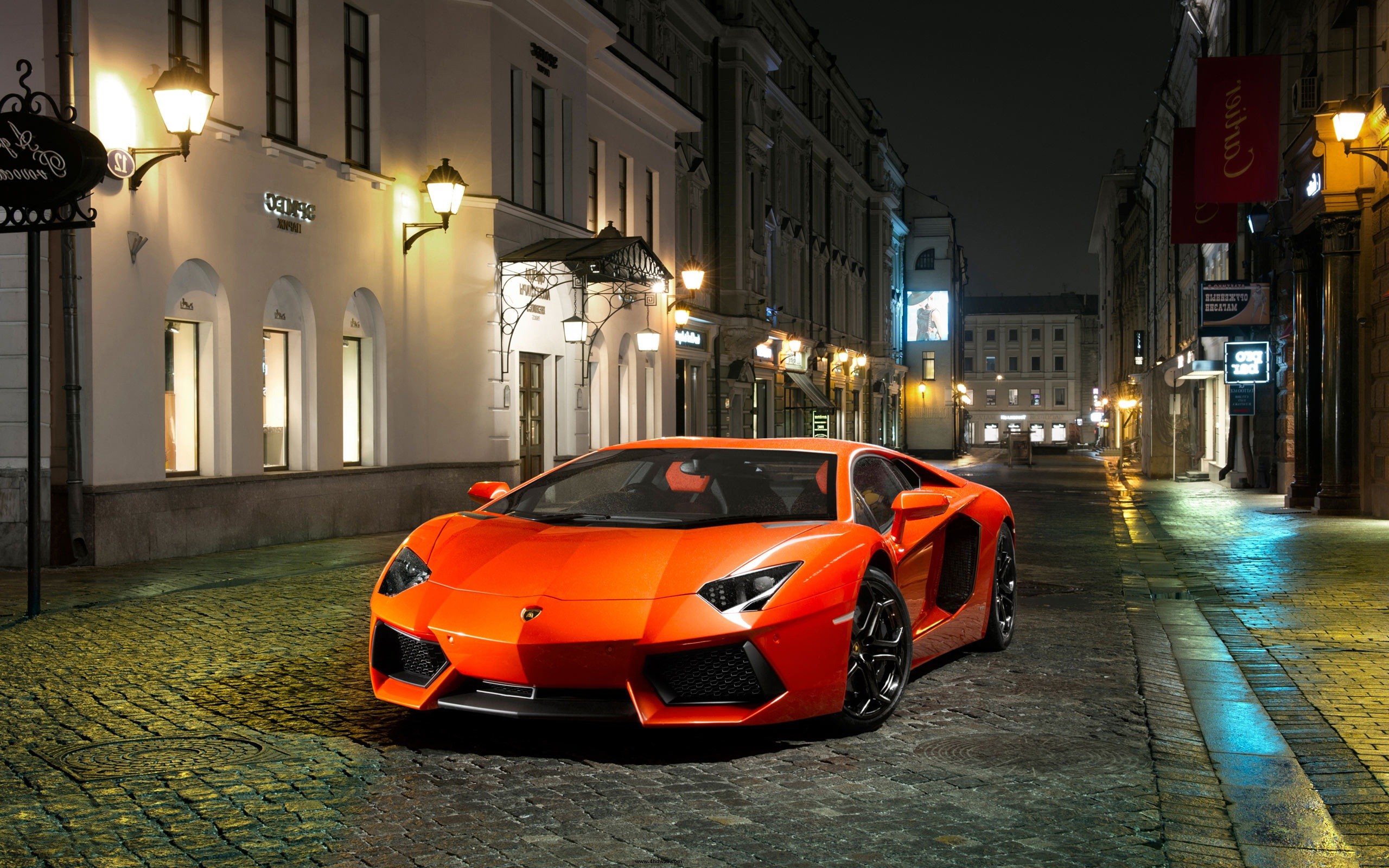 Bright Orange Lamborghini Aventador parked on a cobblestone street at night